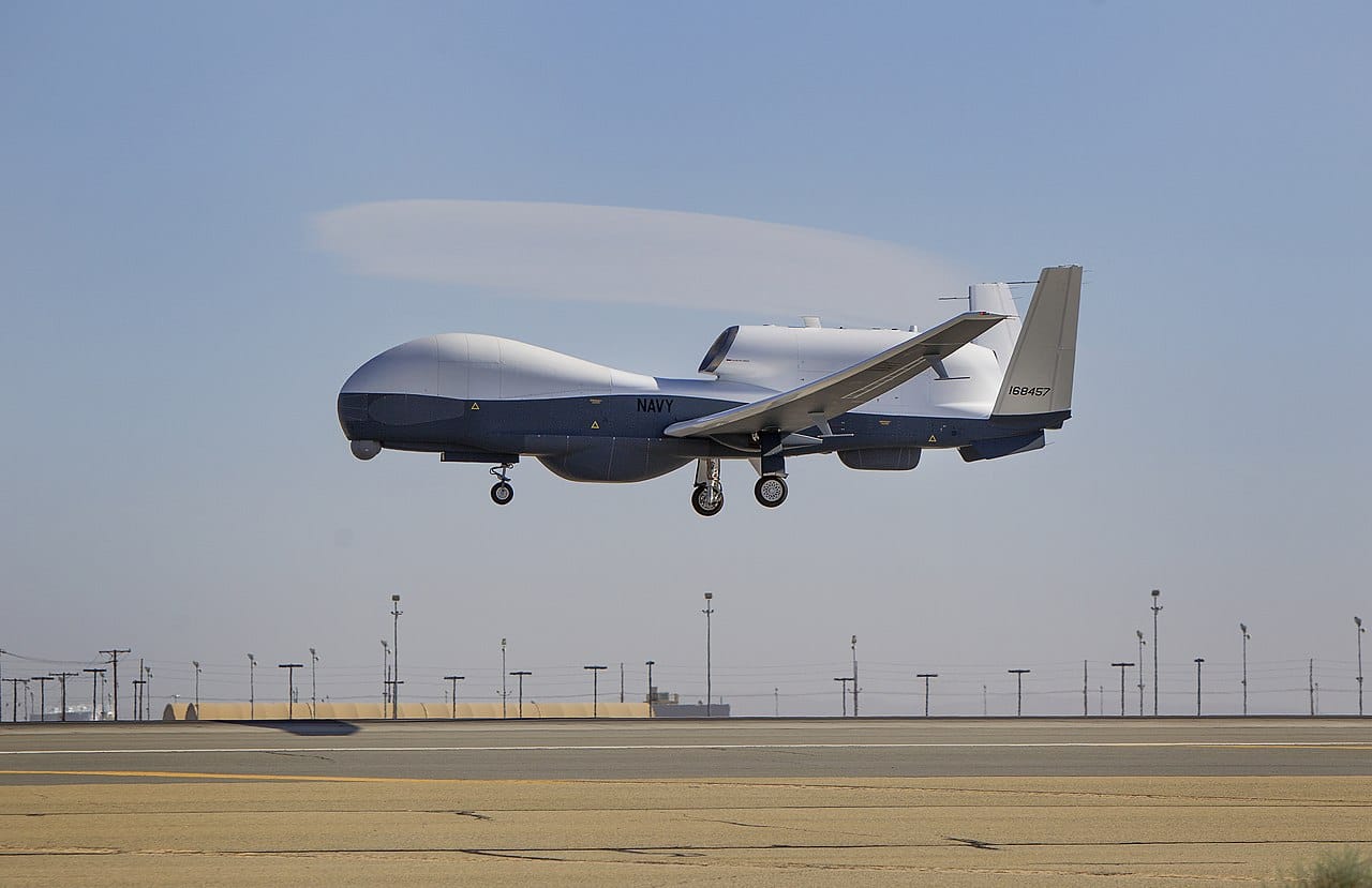 MQ-4C Triton surveillance drone on approach above a desert runway during flight testing.
