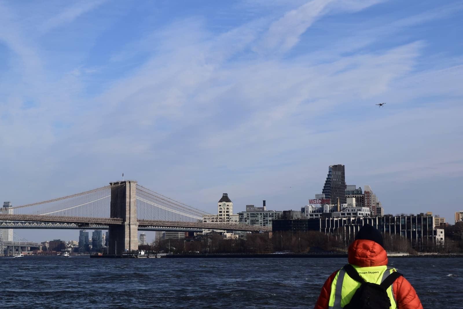 Crew member watches a drone cross the East River toward the Brooklyn Bridge.