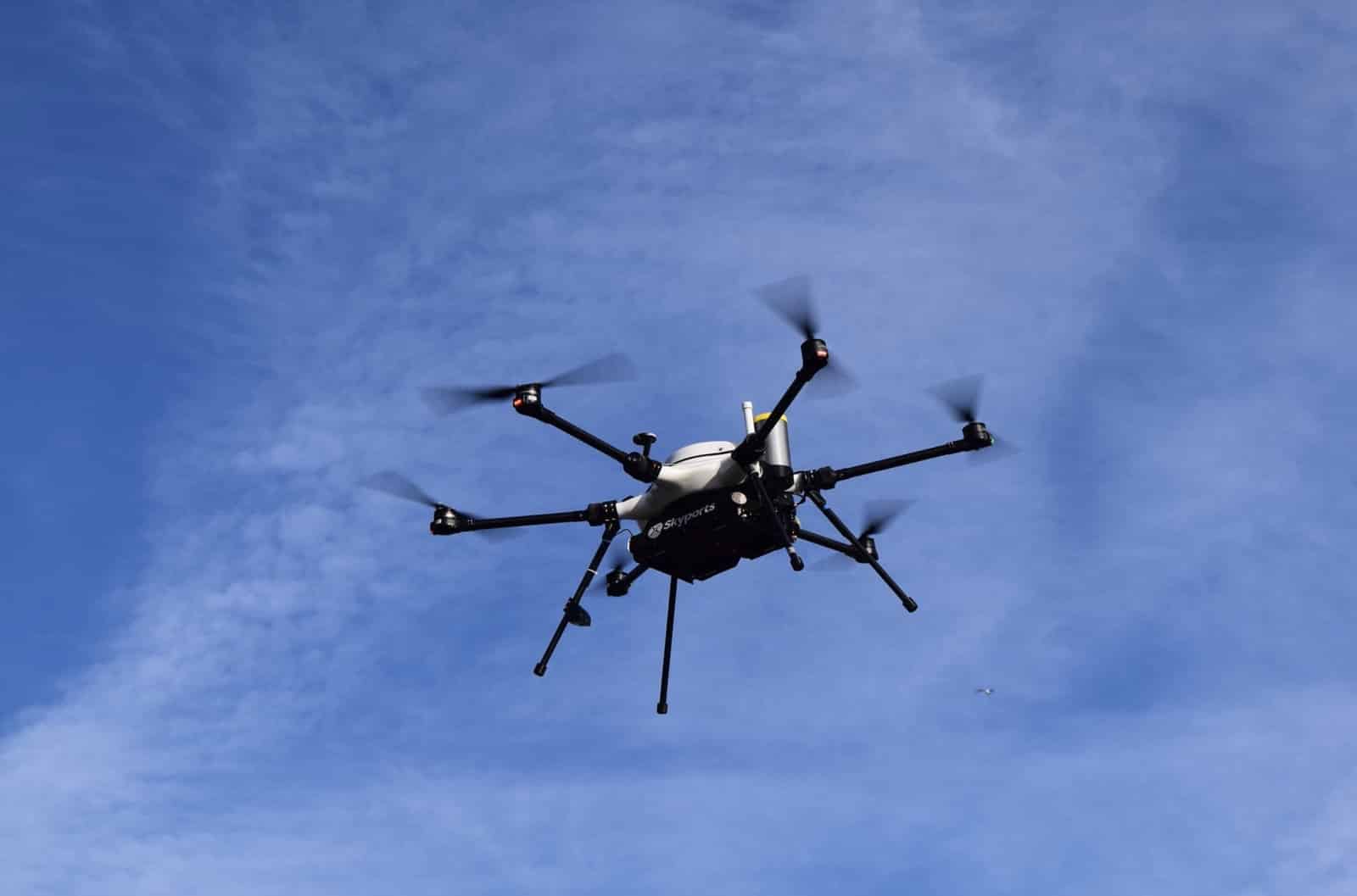Black electric multirotor cargo drone flying against a clear blue sky.