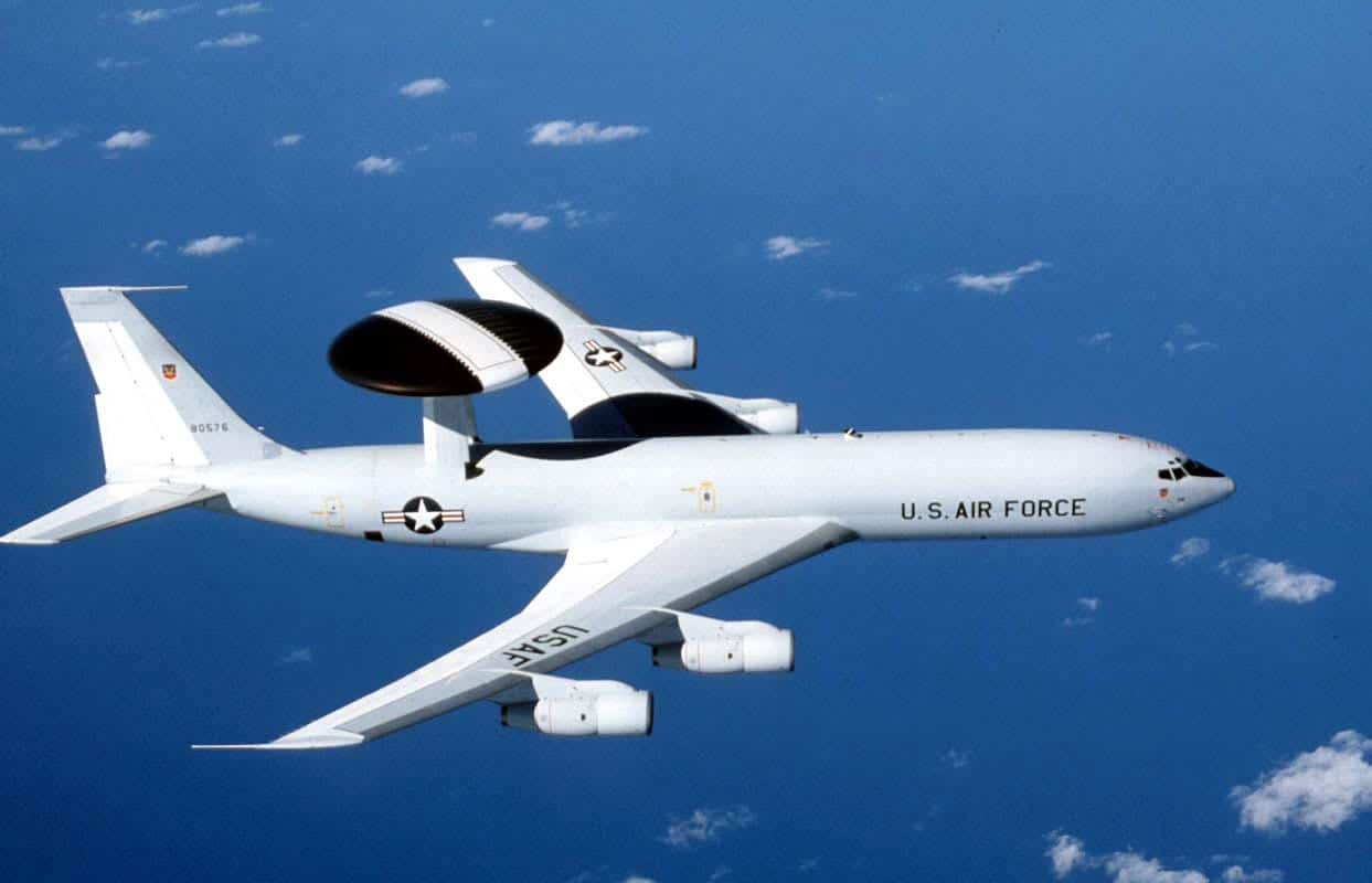 A U.S. Air Force E-3 Sentry AWACS aircraft flying above scattered clouds.