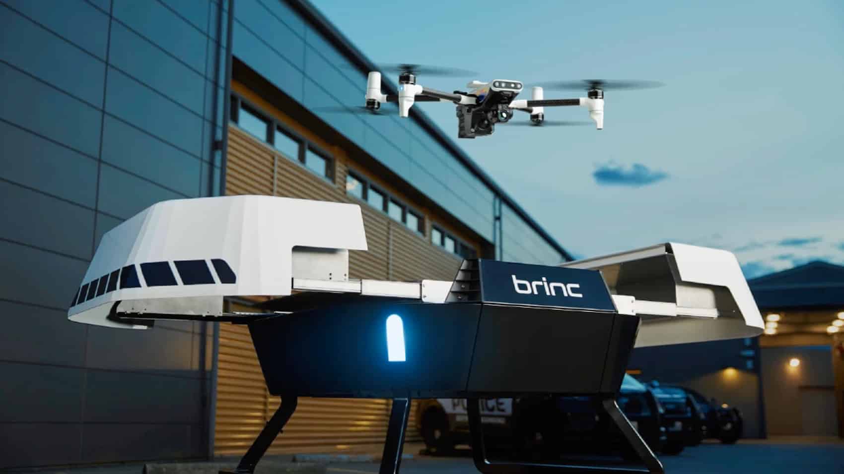 A BRINC drone lifting off from its white dock outside a station as patrol cars wait.