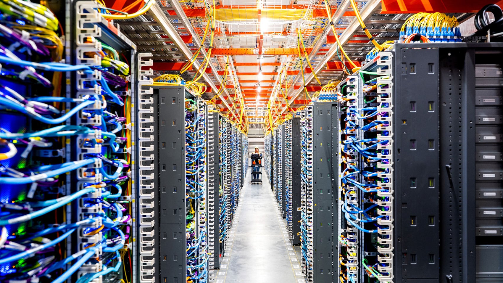 Aisle of server racks and coloured cabling inside a large cloud data center.