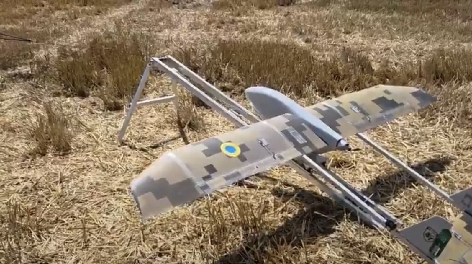 Camouflaged Vidun fixed-wing interceptor resting on dry grass with a Ukrainian roundel.