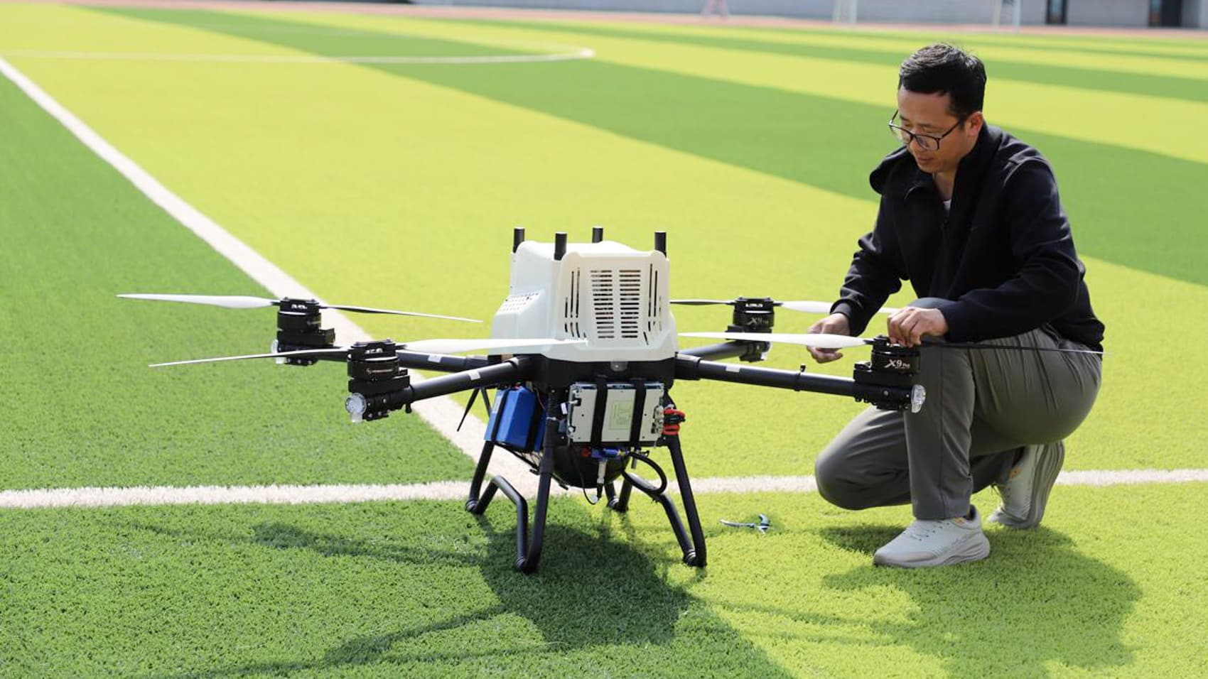 Researcher kneels beside a large hydrogen-powered industrial multirotor on a sports field.