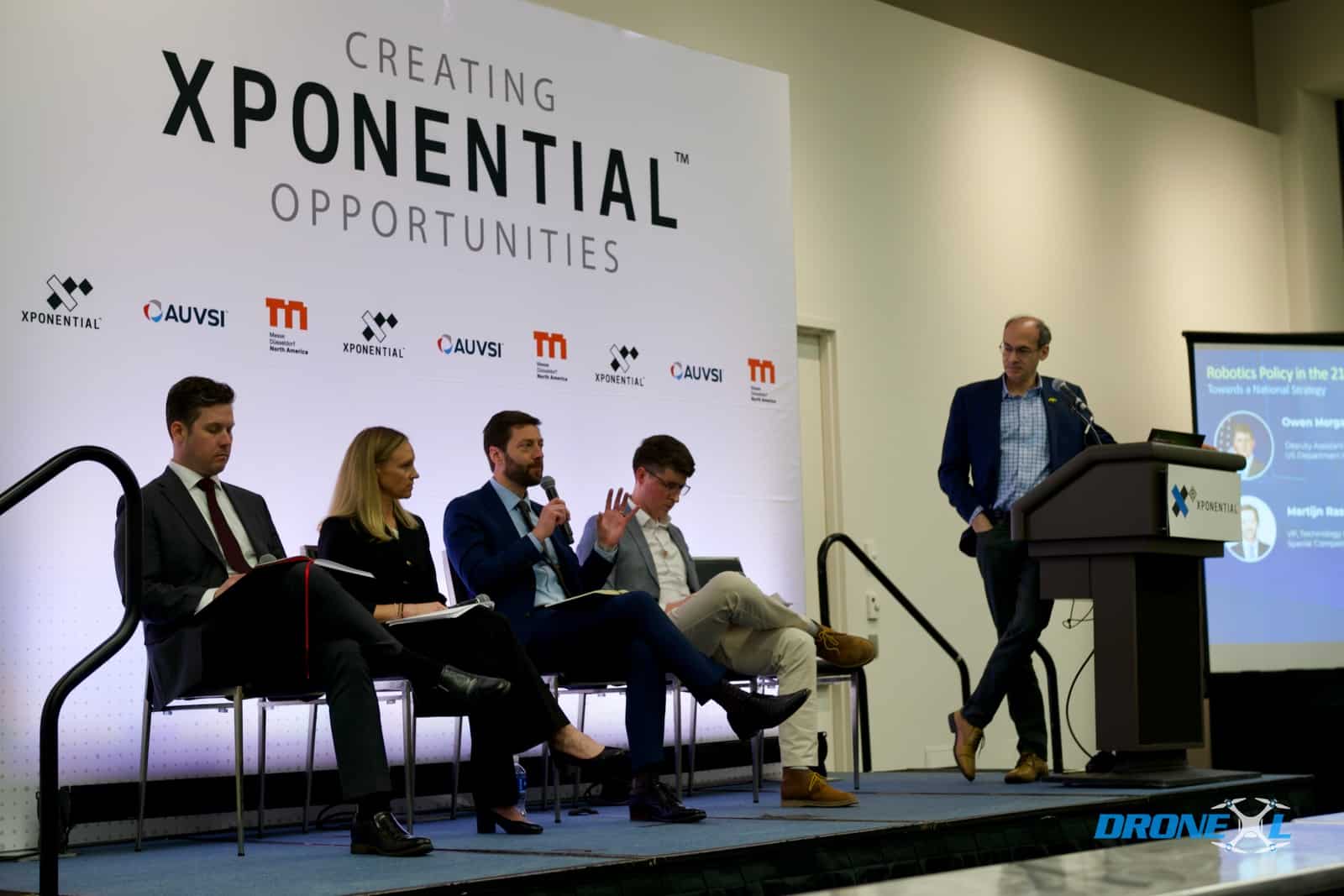 Four panelists sit onstage while Brendan Schulman moderates from the XPONENTIAL Detroit podium.
