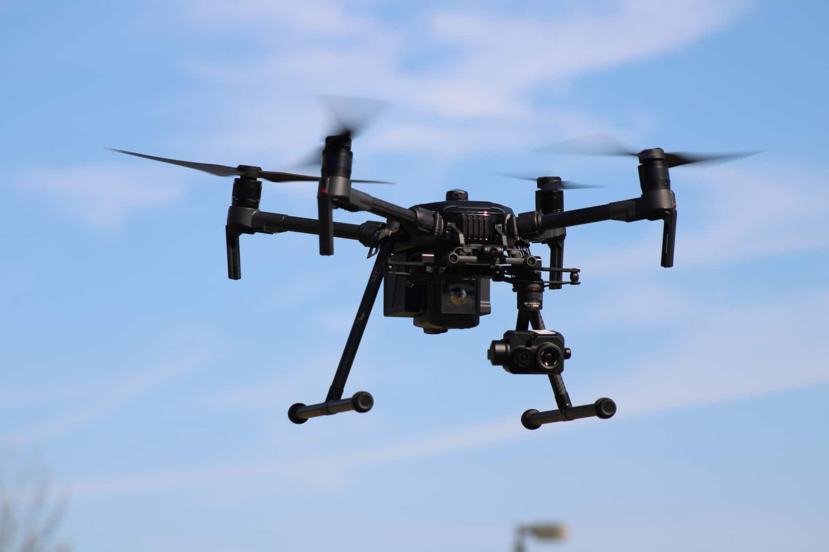 DJI Matrice 210 in flight with dual gimbal cameras under a blue sky.