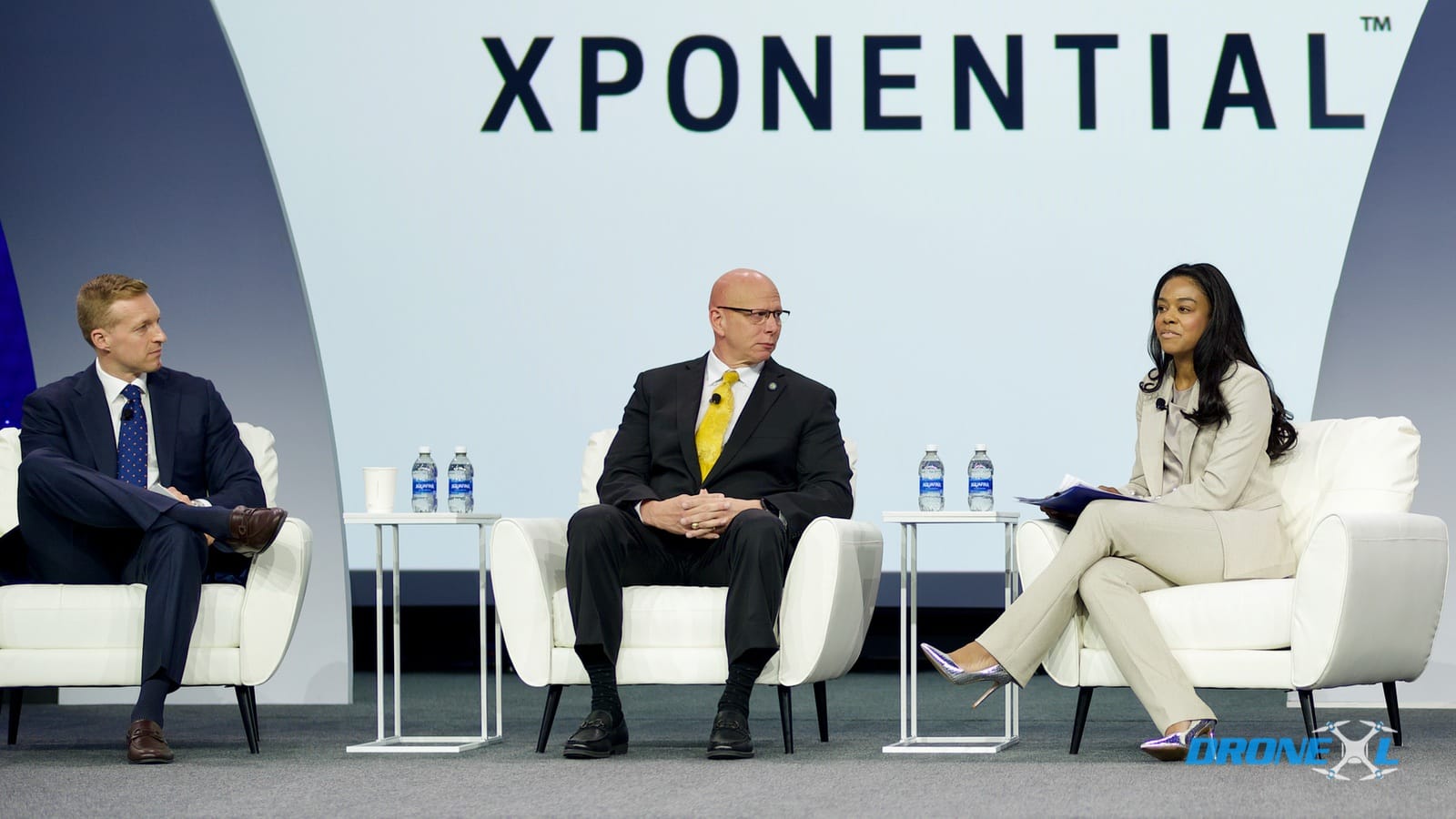 Three panelists seated on stage beneath a large XPONENTIAL banner.