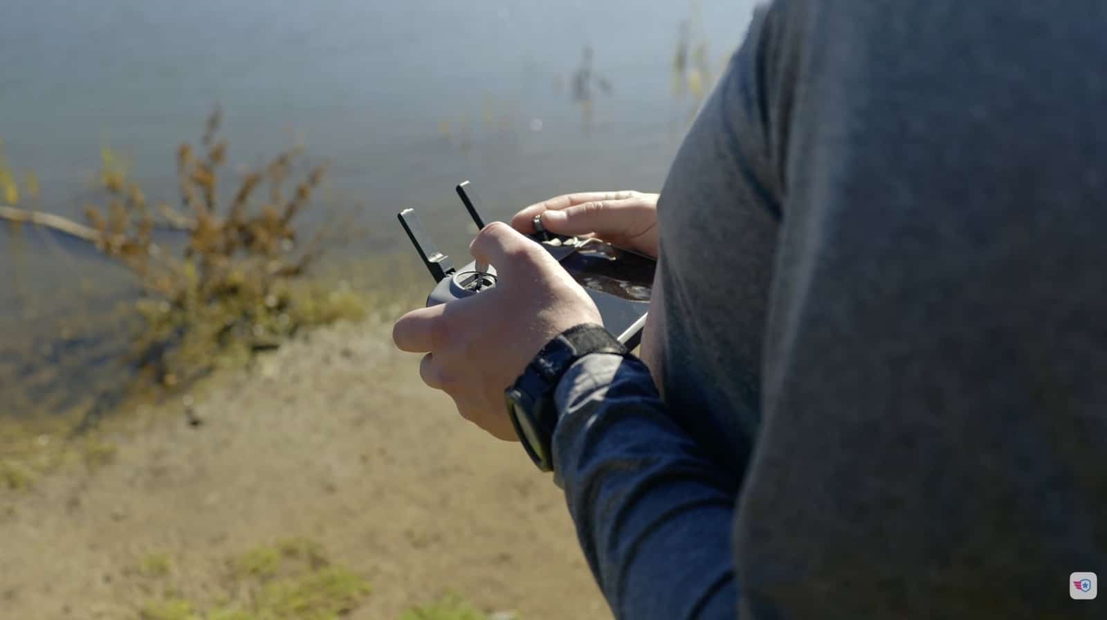 Close-up of a pilot's hands on the controller near the shoreline.