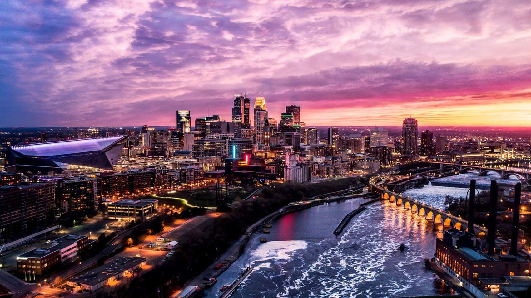 Aerial dusk view of the Minneapolis skyline and river under a pink sky.