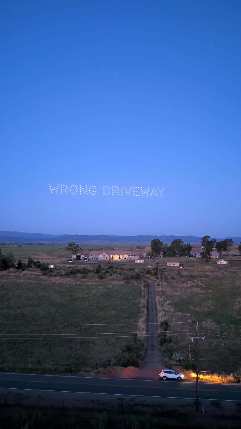 Drone lights spell WRONG DRIVEWAY above Tom BetGeorge's rural California property at dusk.