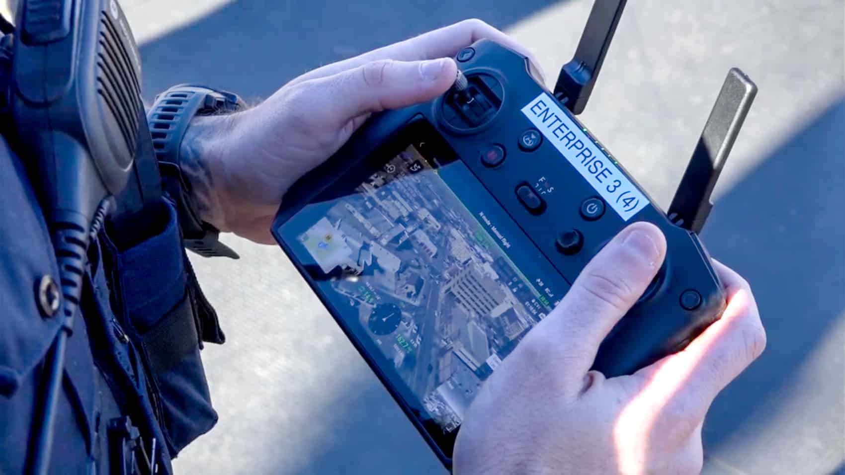 A police officer holds a DJI enterprise smart controller showing a live aerial map.