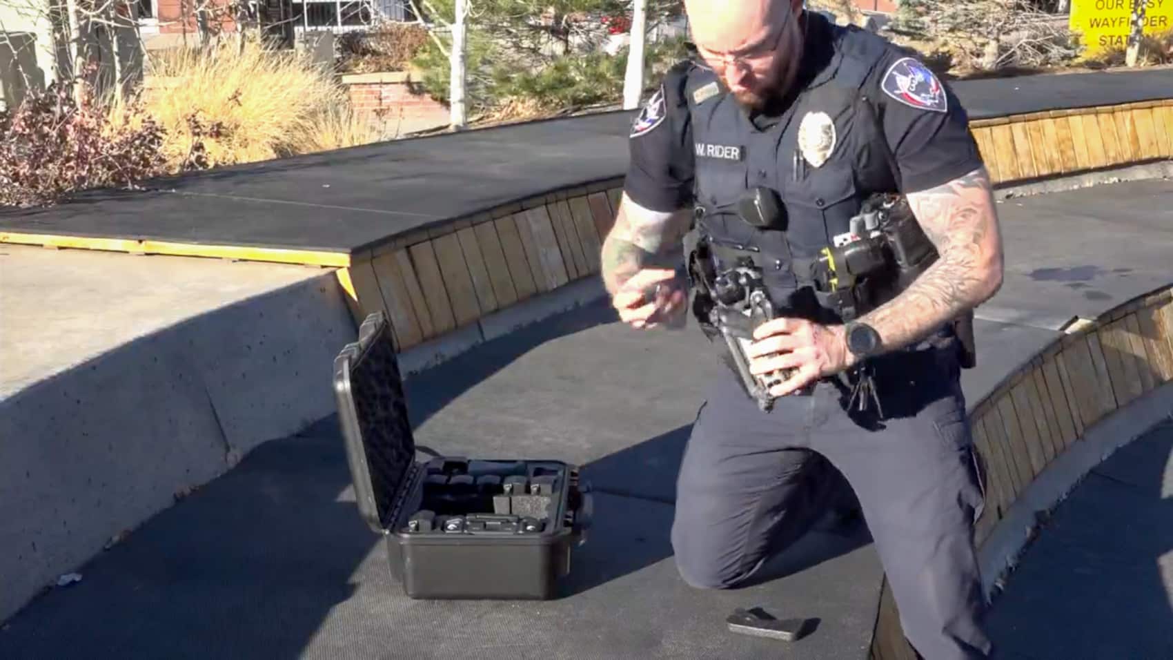 A Wyoming police officer unfolds a drone beside an open hard case on pavement.