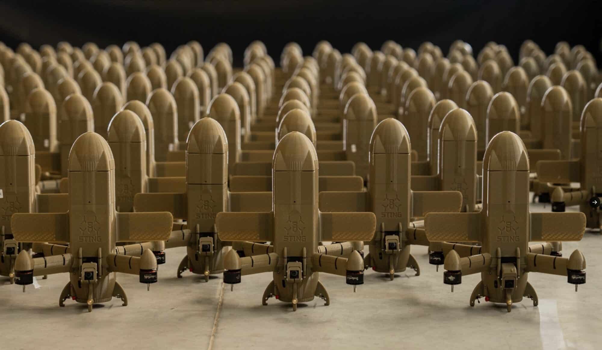 Rows of tan fixed-wing interceptor drones lined up on a warehouse floor.