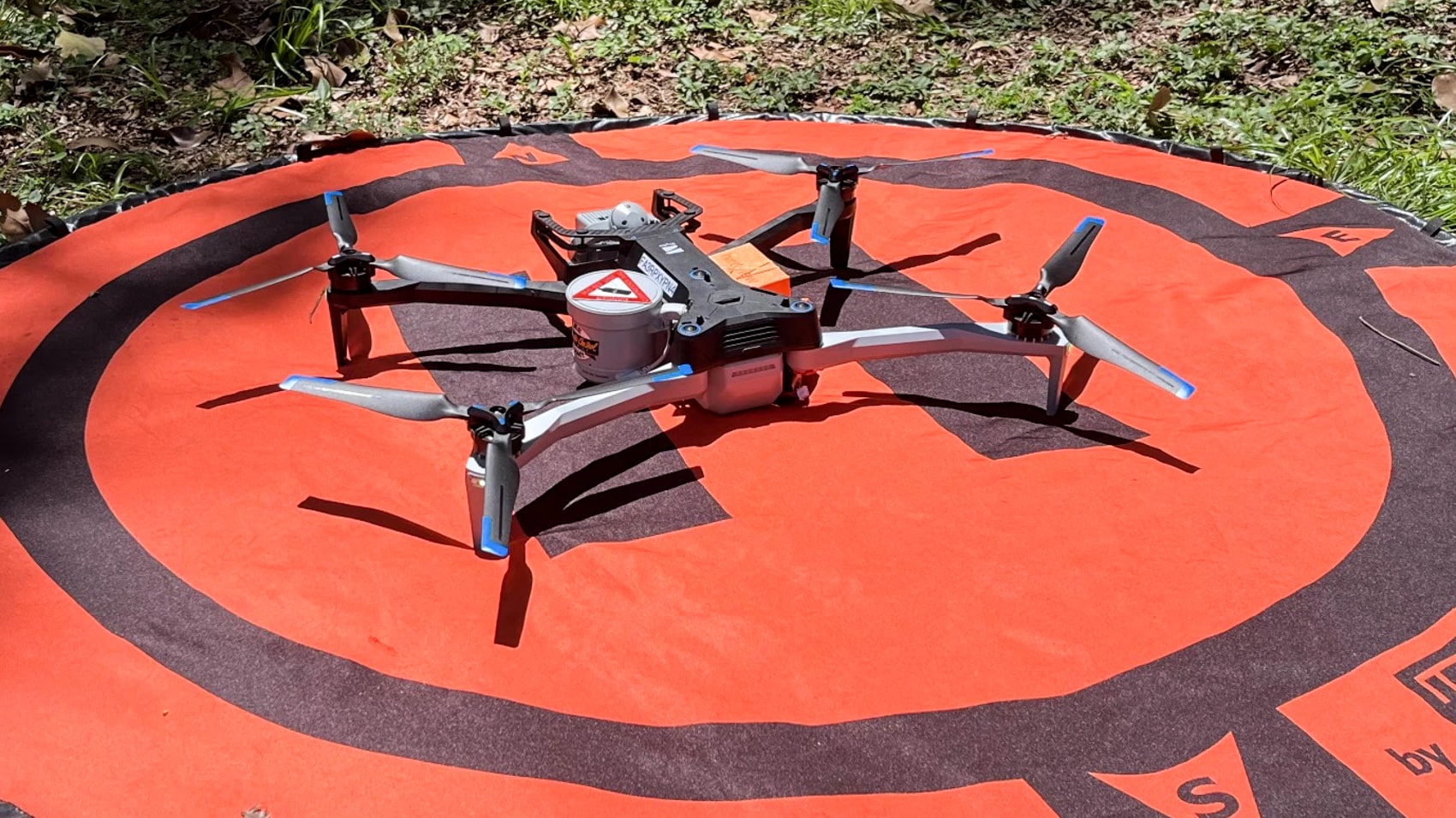 Skydio X10 quadcopter parked on an orange landing pad in wooded terrain.