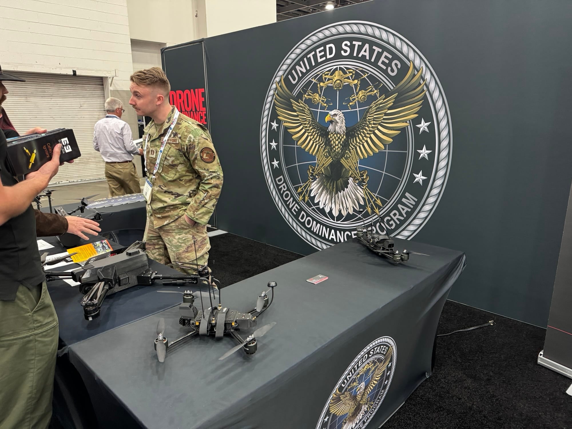 Visitors inspect small quadcopters at a booth backed by a Drone Dominance Program seal.