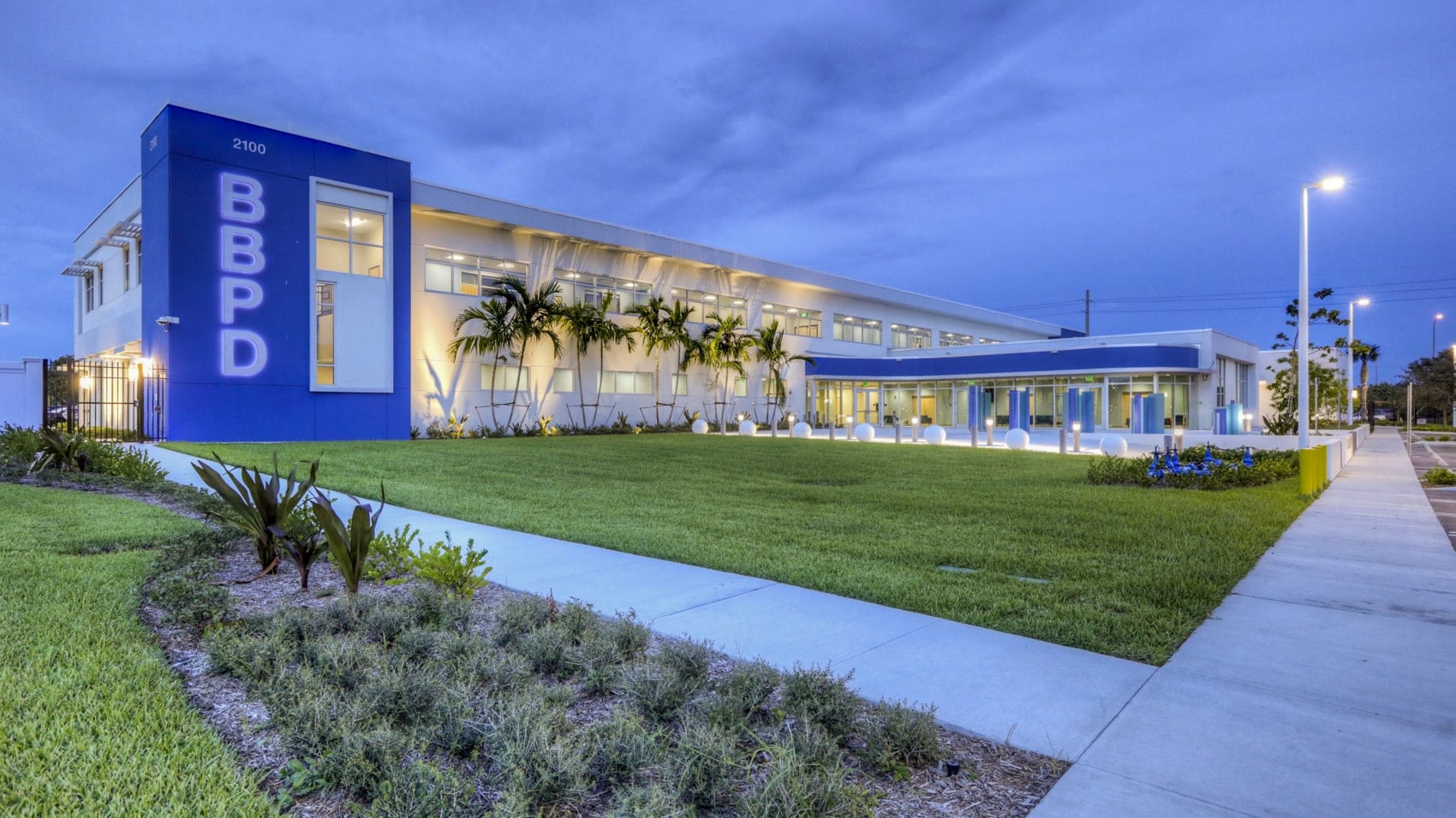 Boynton Beach Police Department headquarters lit blue at dusk behind a manicured lawn.