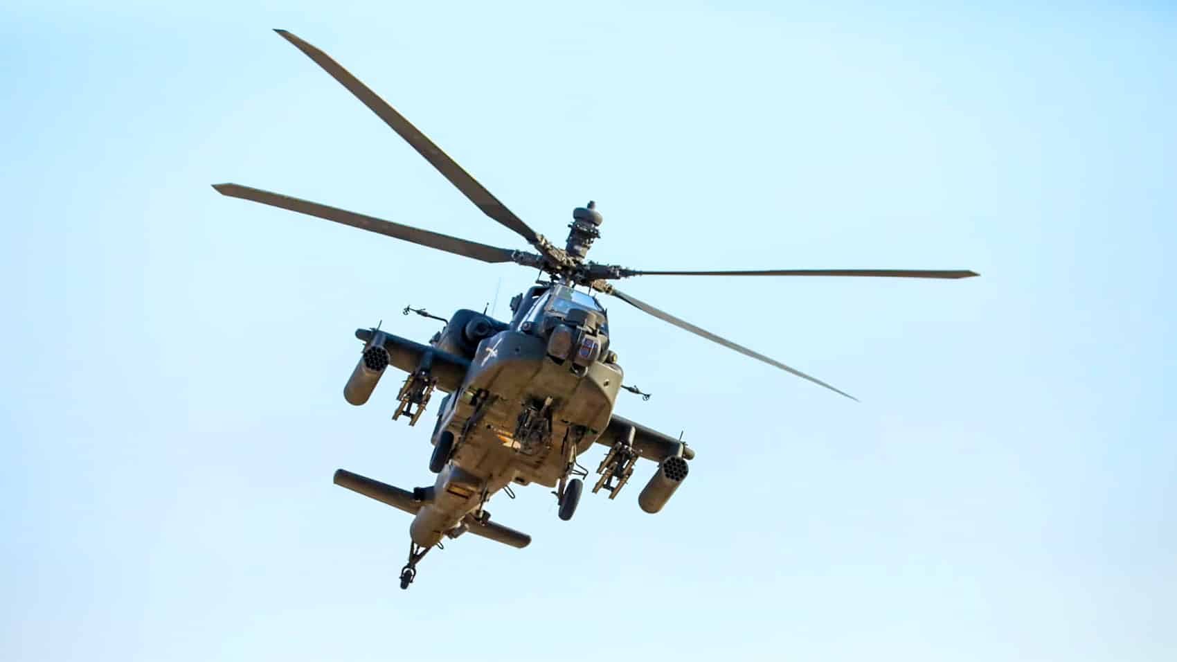AH-64 Apache attack helicopter flying head-on against a pale sky.