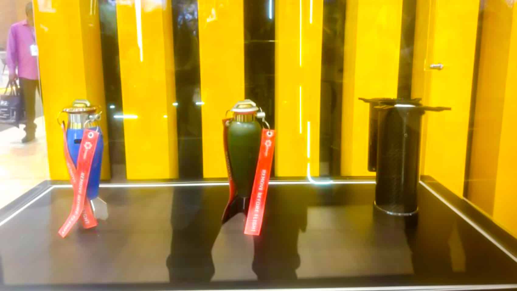 Three ribbon-tailed drone grenades and a launch tube displayed at a defense expo.
