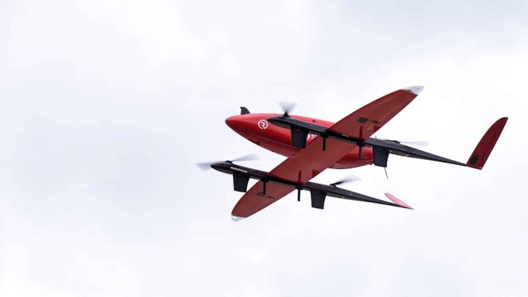 The red RigiTech Eiger cruising in wing-borne flight under an overcast sky.