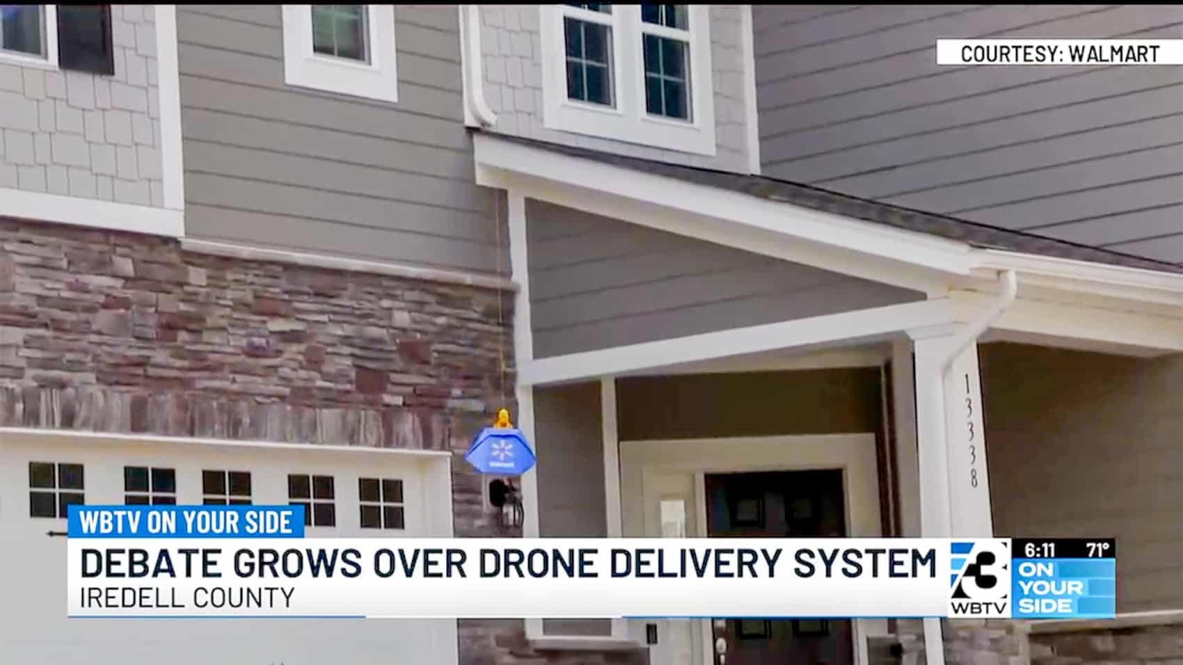 News footage of a delivery drone lowering a package by tether above a house.