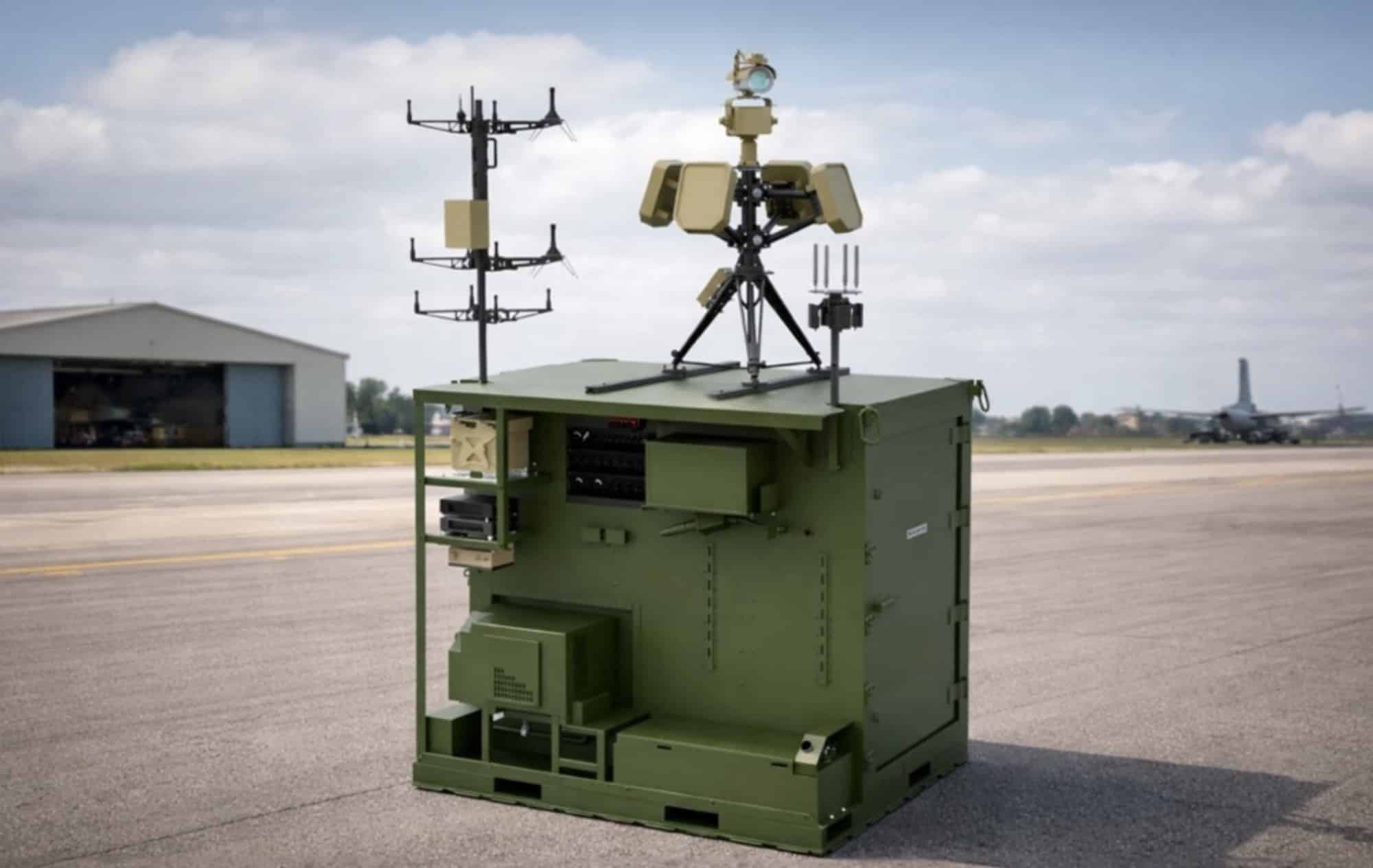 Green militarized shelter topped with radar and sensor masts on an airfield apron.