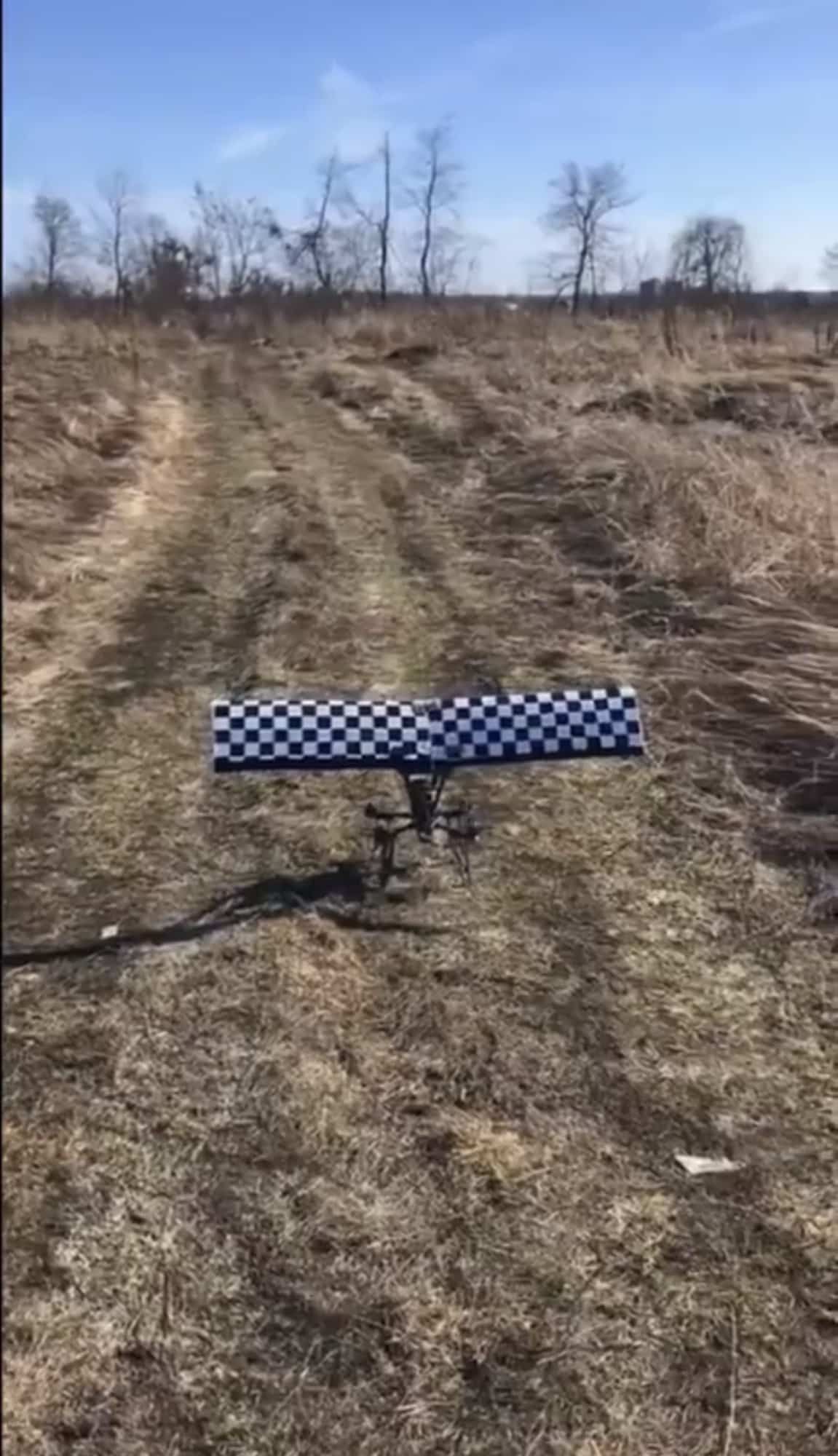 Checkered wing bolted to an FPV drone sitting on a rutted dirt track.