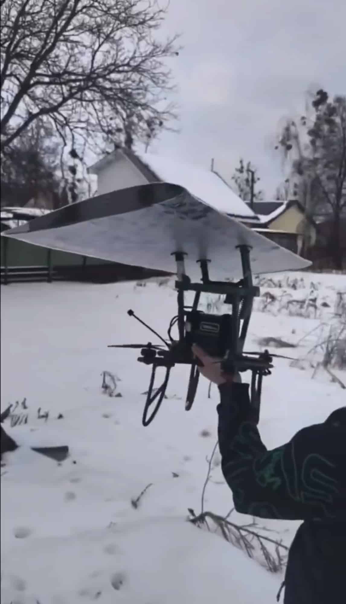 Soldier lifting a quadcopter fitted with a large detachable wing in snow.