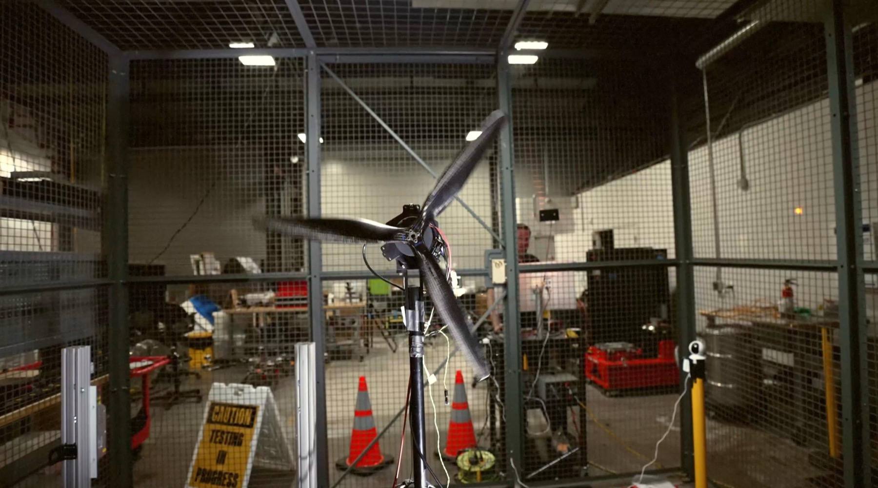 Large carbon fiber drone propeller spinning on an instrumented test stand inside a protective enclosure