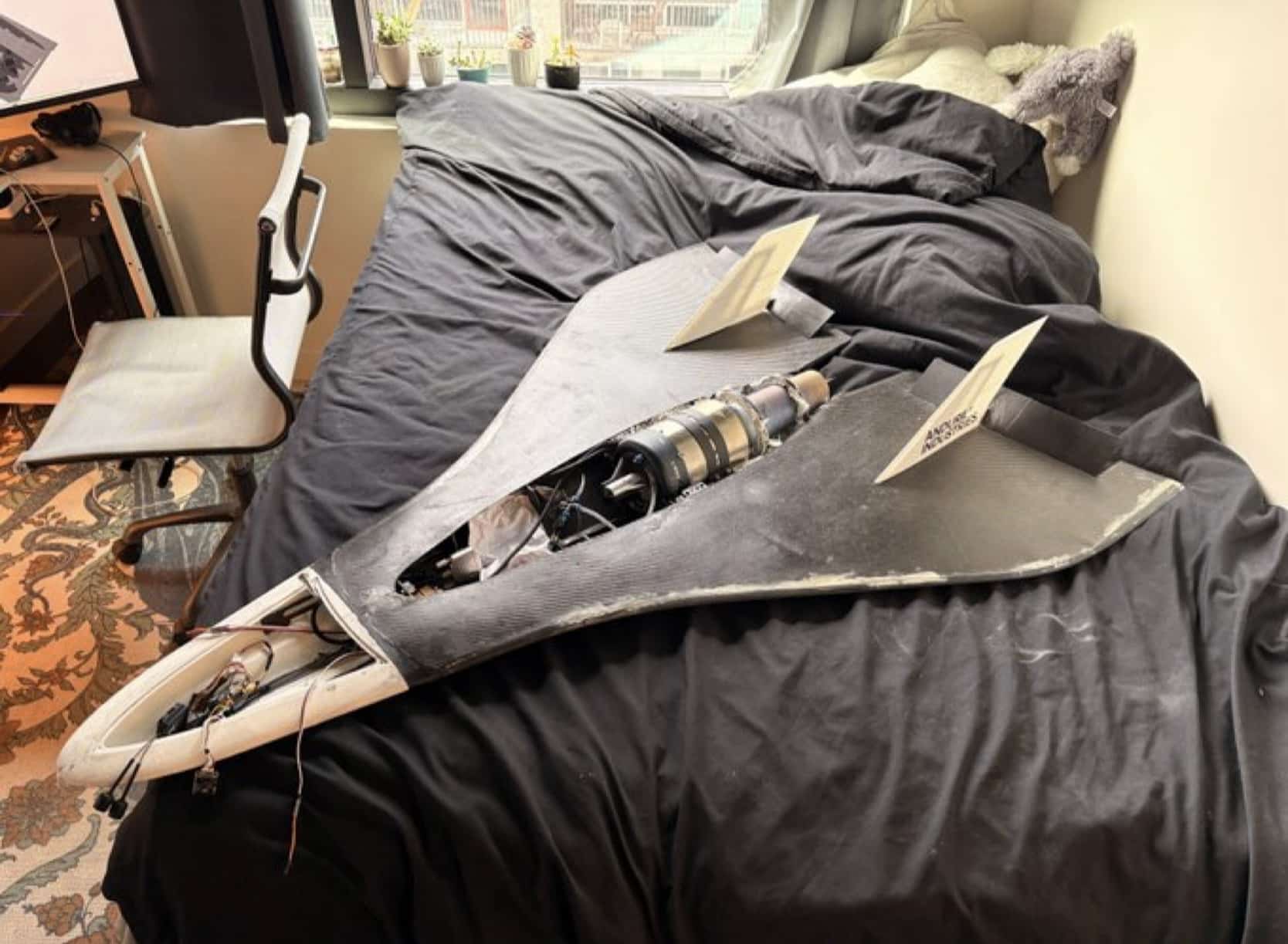 Homemade black delta-wing jet aircraft resting on an unmade dorm room bed.