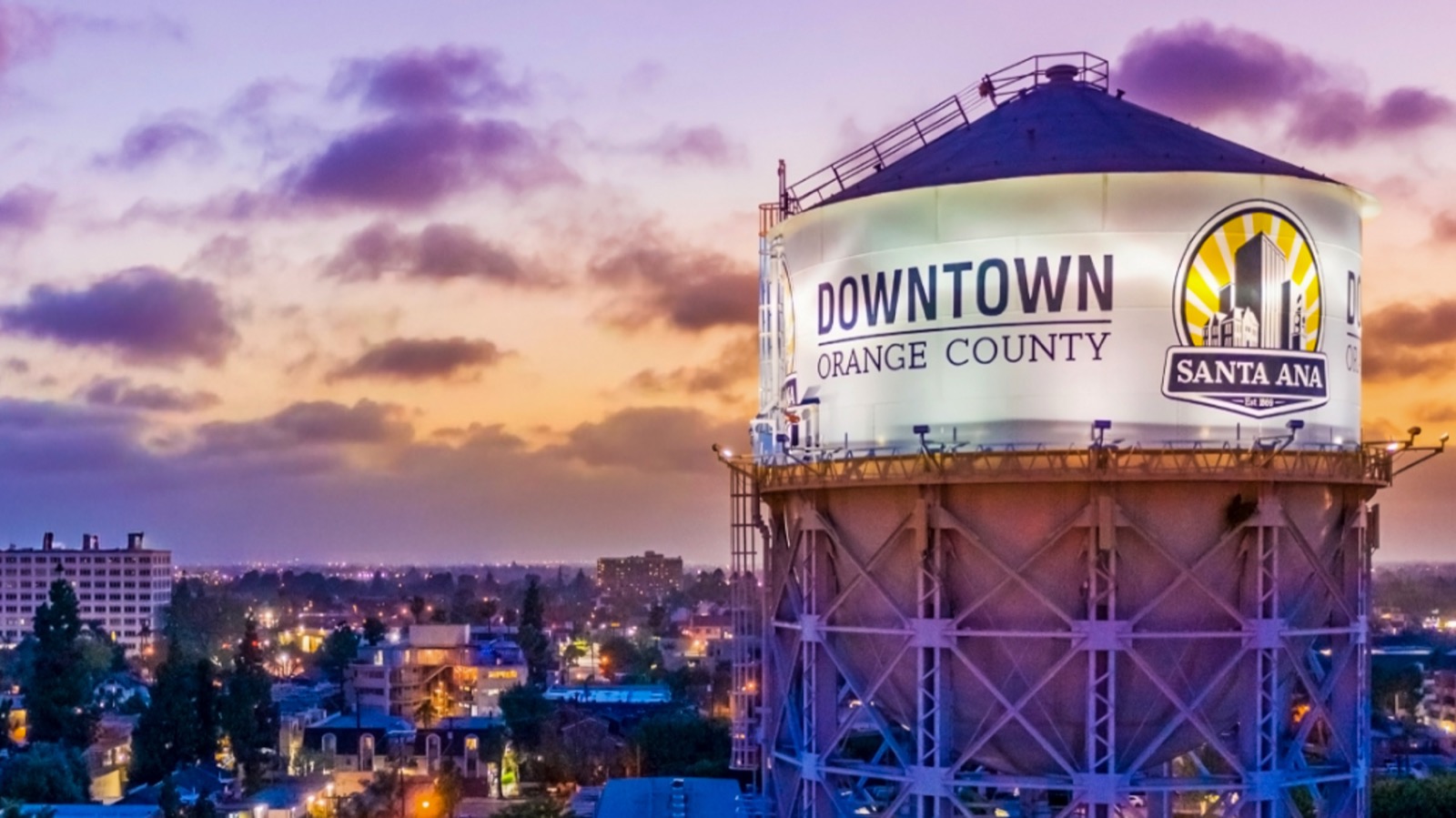 Downtown Orange County and Santa Ana logos illuminated on a water tower at sunset