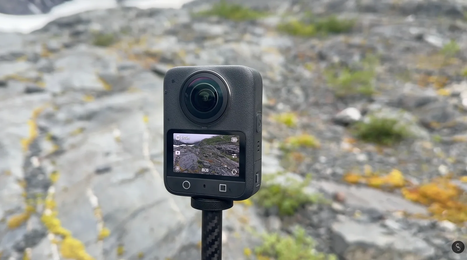 360-degree action camera mounted on an invisible selfie stick, screen showing 8K30 recording mode against a rocky alpine backdrop