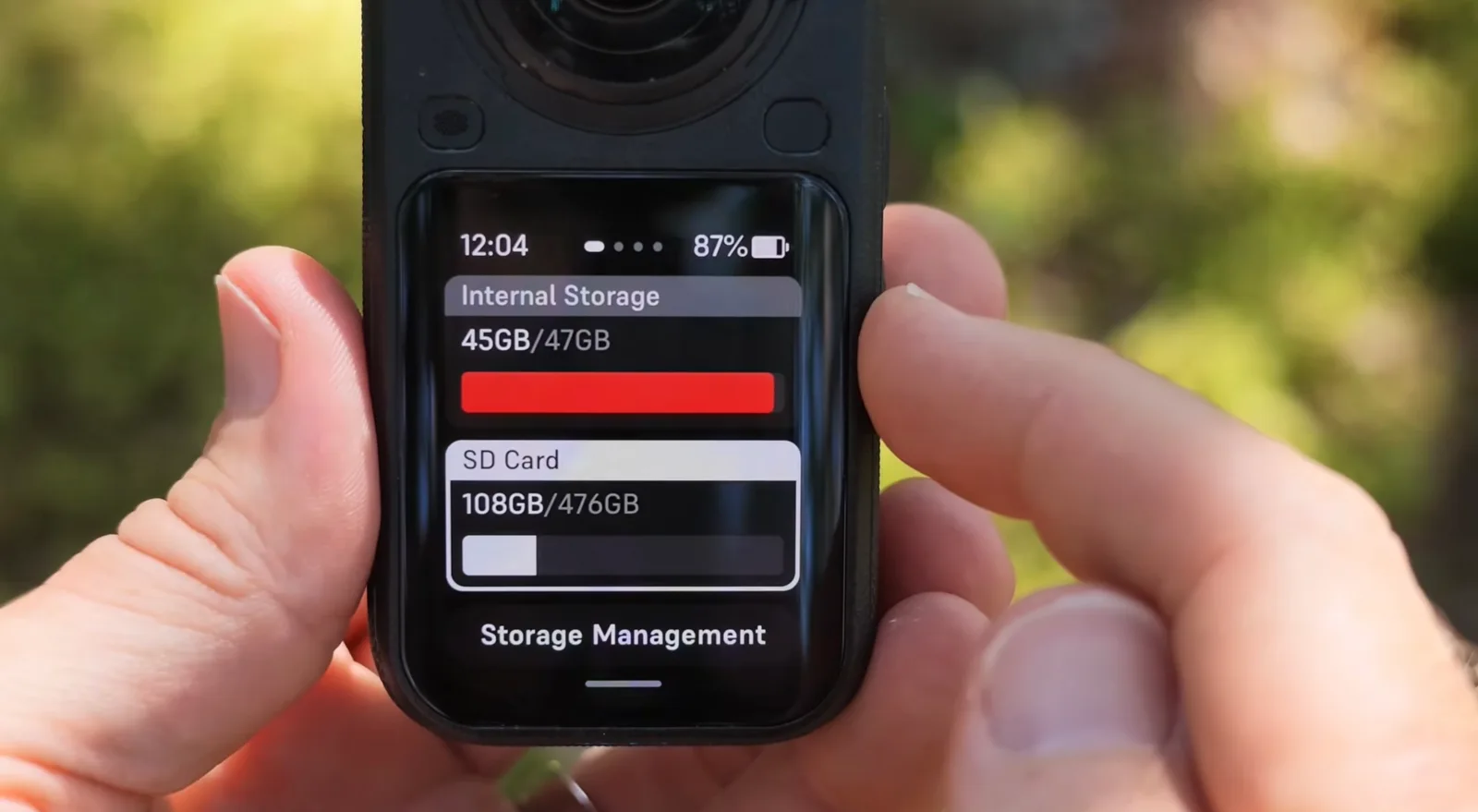 Hands holding a 360-degree action camera showing its Storage Management screen with internal storage at 45GB of 47GB and an SD card at 108GB of 476GB.