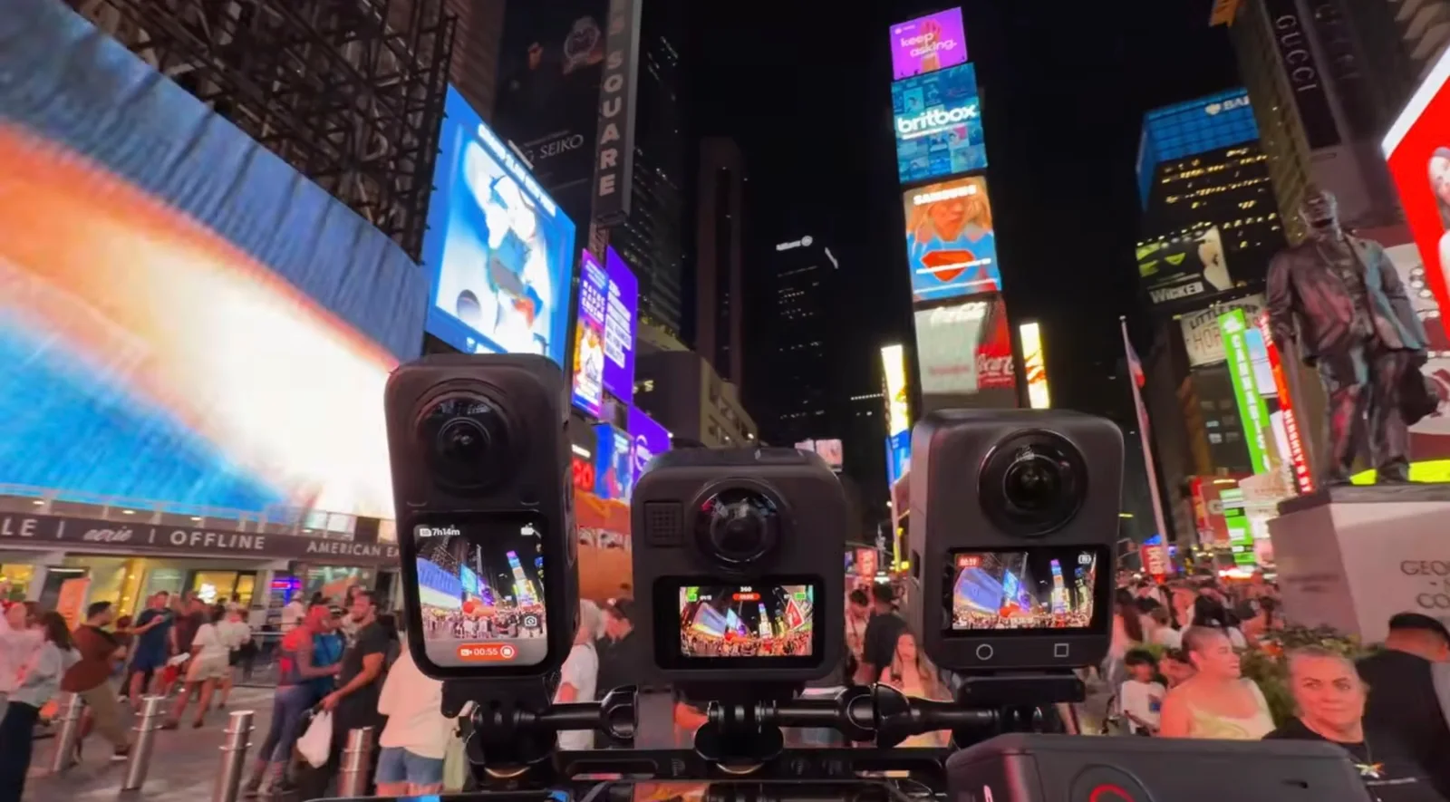 Three 360-degree action cameras mounted side by side on a rig, recording in Times Square at night with illuminated billboards behind them