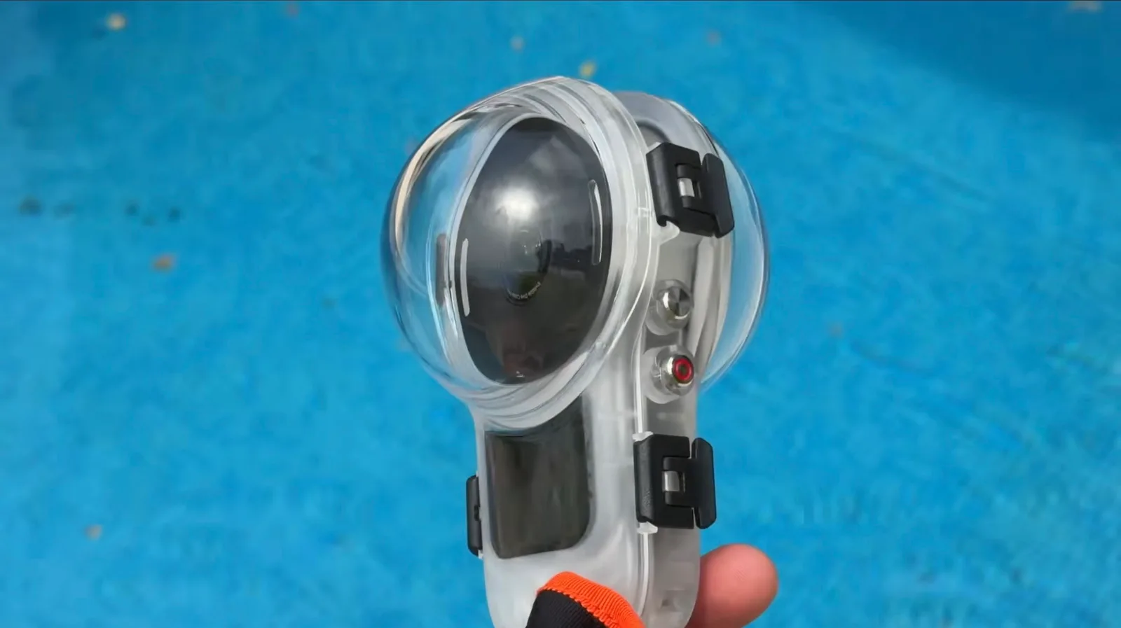 Action camera sealed inside a clear waterproof dive case with a domed lens port, held above blue pool water