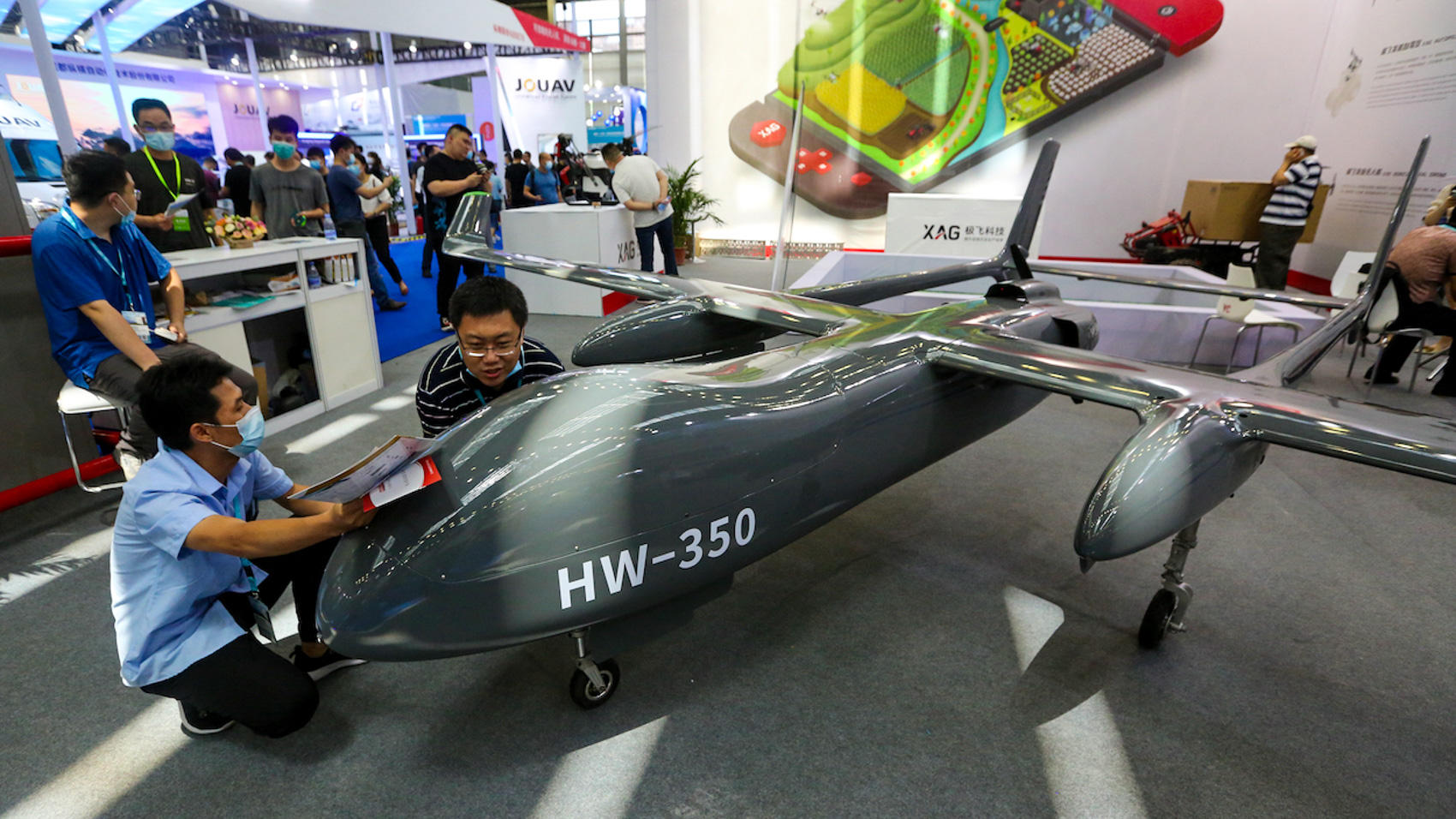 Exhibition staff position a large grey twin-boom uncrewed aircraft marked HW-350 on the show floor of a drone trade fair in Shenzhen, China.