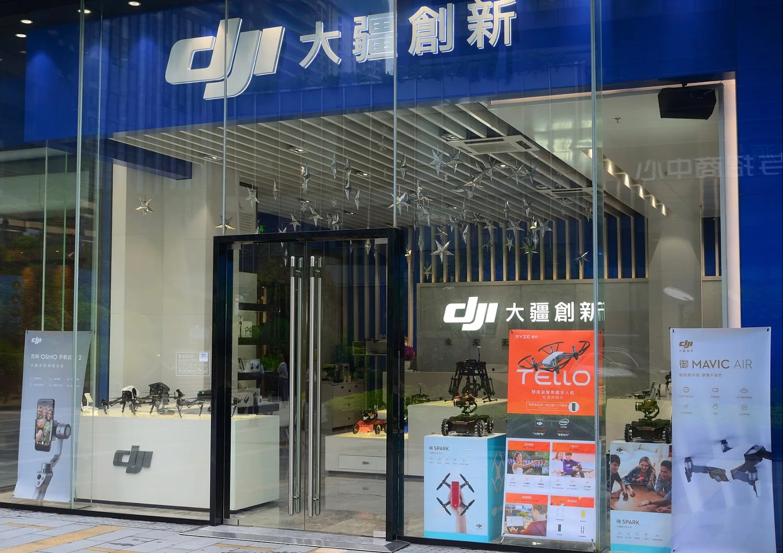 Glass storefront of a DJI flagship store in Shenzhen with the DJI logo and Chinese name above the entrance and Tello, Spark and Mavic Air posters in the window