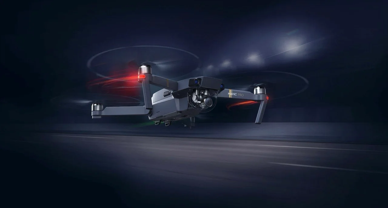 DJI Mavic Pro folding drone hovering in flight at night with propellers spinning and navigation lights lit