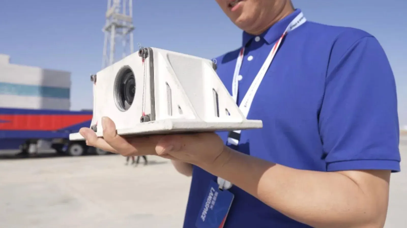 A LandSpace engineer in a blue polo holds a scorched white ceramic camera housing containing a DJI Osmo Action 6 at a desert launch site