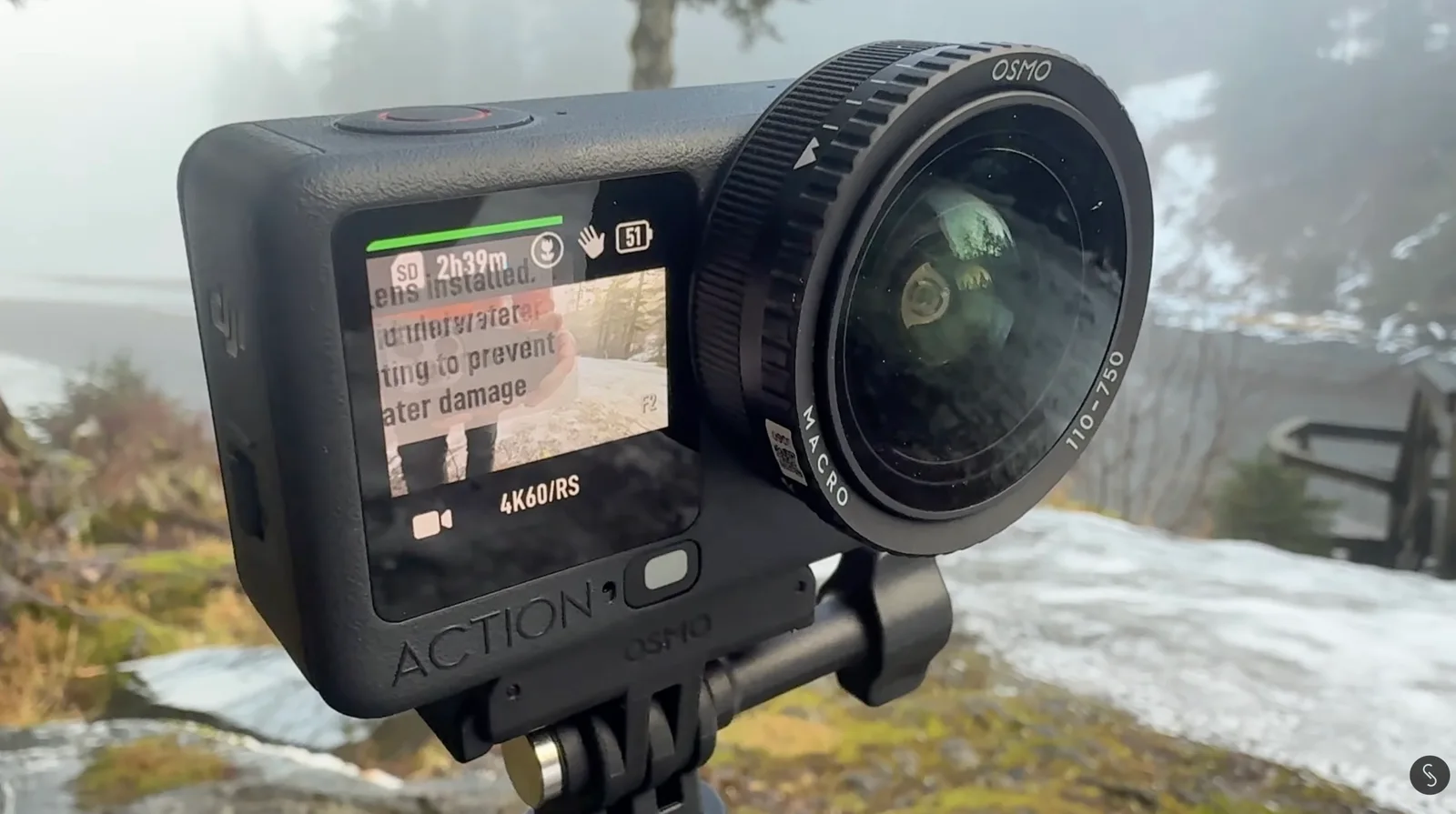 DJI Osmo Action camera fitted with a screw-on Osmo macro lens, mounted on a tripod above a foggy, snow-dusted coastal overlook