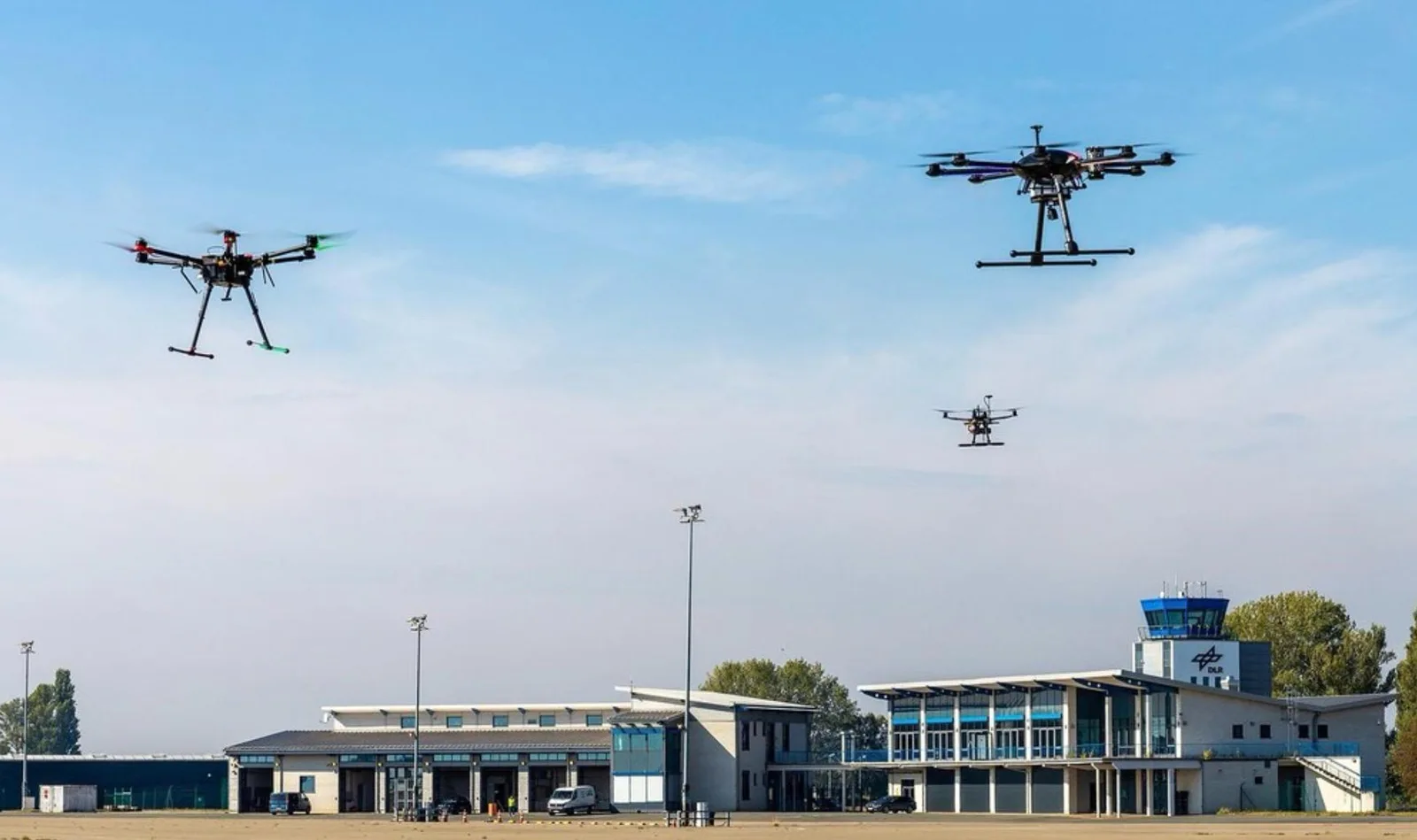 Three multirotor drones hovering above the apron at Magdeburg-Cochstedt Airport in front of the DLR terminal and control tower