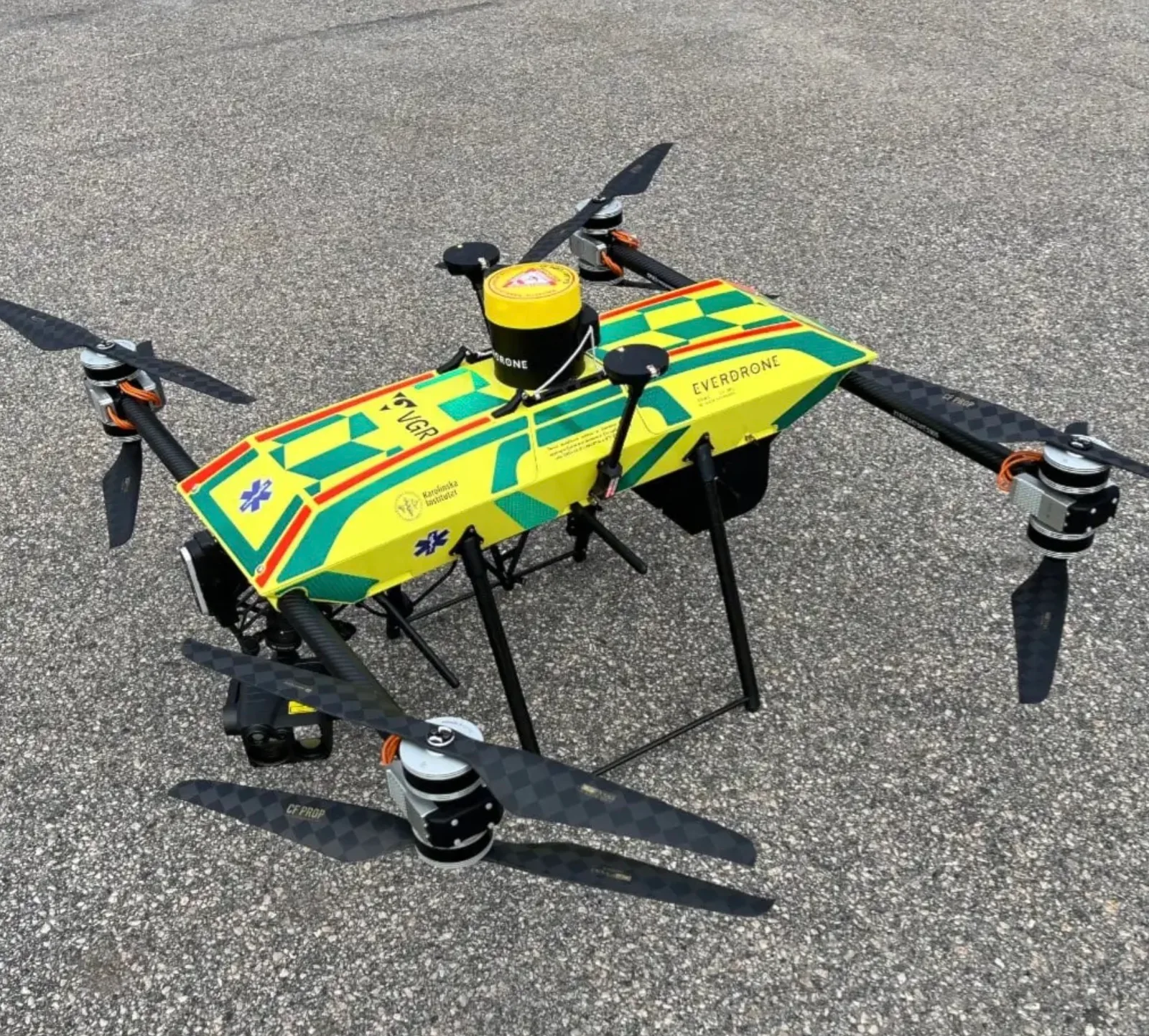 Everdrone's yellow and green emergency drone with hi-vis ambulance livery, VGR and Karolinska Institutet markings, on an asphalt surface