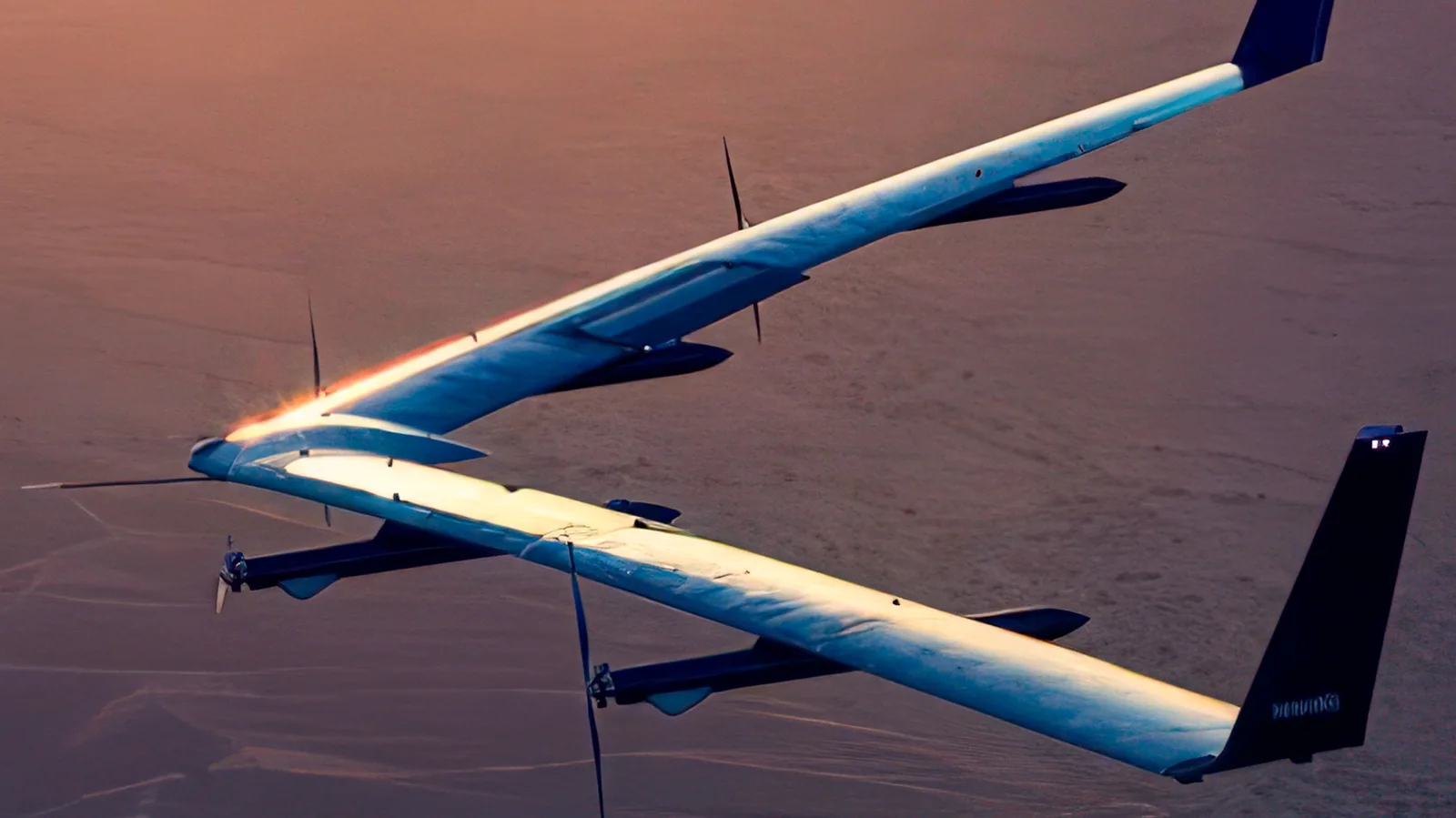 Facebook's Aquila solar-powered internet drone in flight at low altitude over desert terrain, its long slender wing lit along the leading edge by low sun