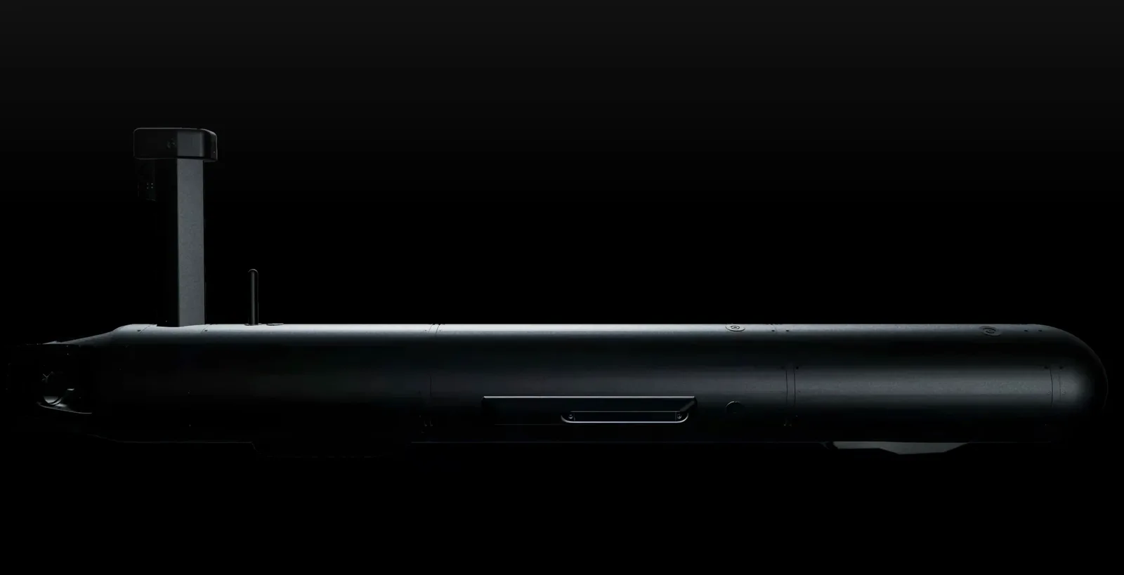 Side profile of the Ghostfin autonomous underwater drone, a long black torpedo-shaped hull with a tall mast and antenna, against a black background.