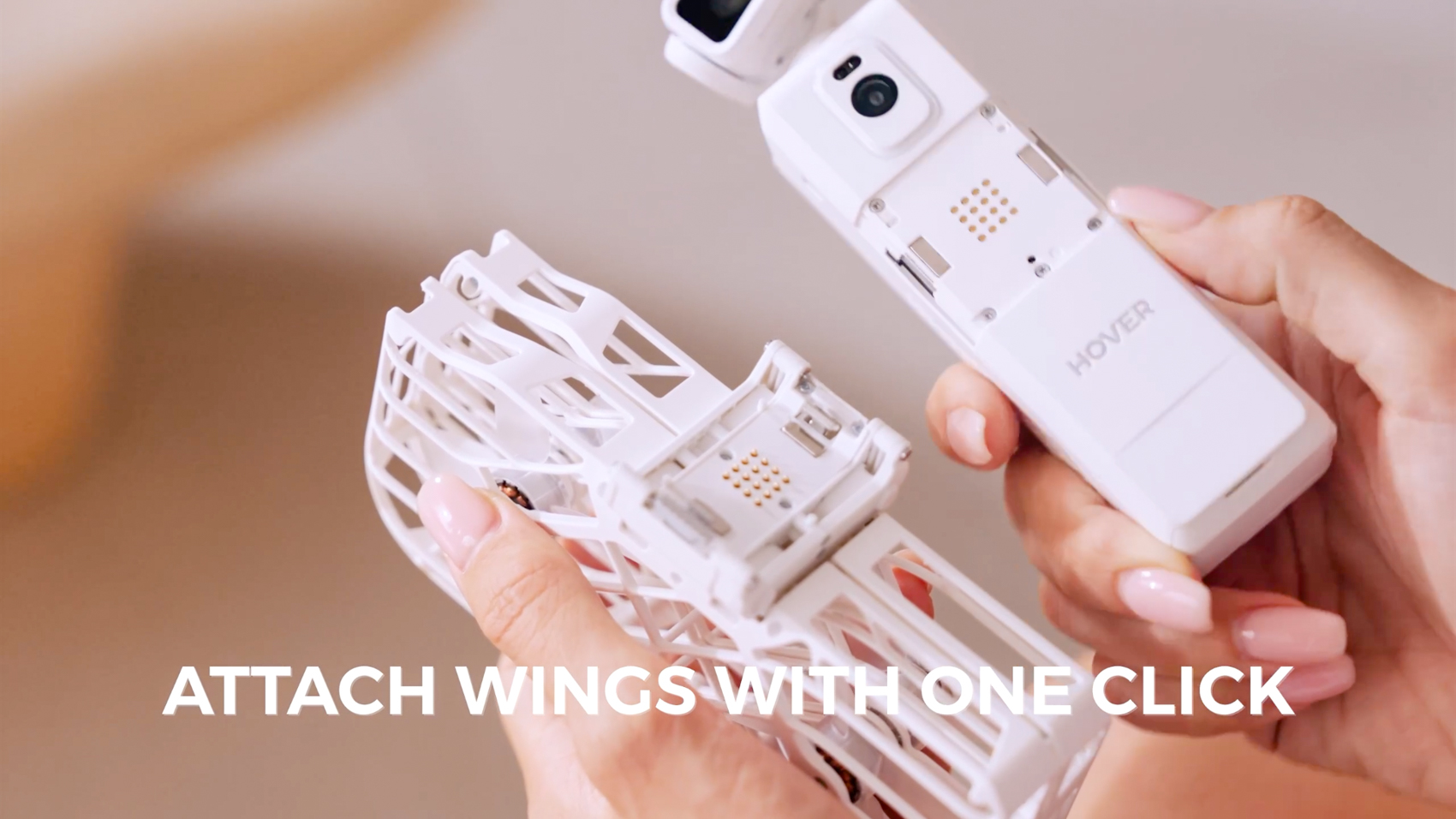 Hands hold the VERSA camera above its propeller carrier, exposing the latch hardware and gold contact pads, with the caption 'Attach wings with one click'