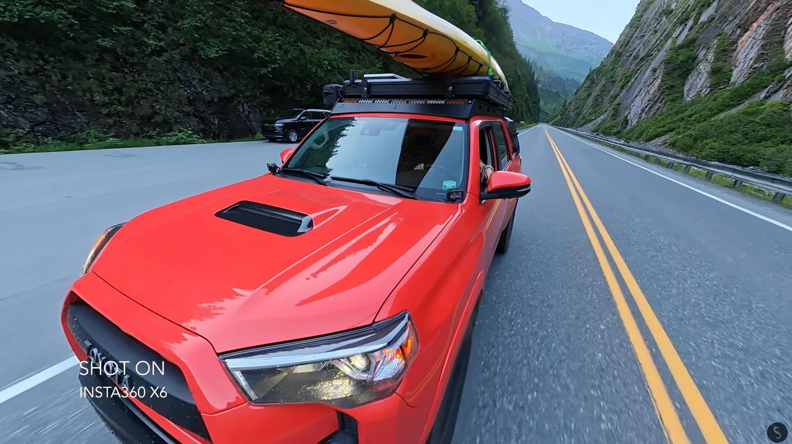Red Toyota 4Runner with a yellow kayak strapped to its roof rack driving through a mountain pass, captured by an Insta360 X6 360-degree camera