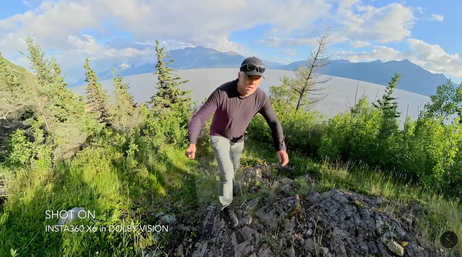 Hiker climbing a rocky ridge trail above a glacial valley, shot on an Insta360 X6 in Dolby Vision