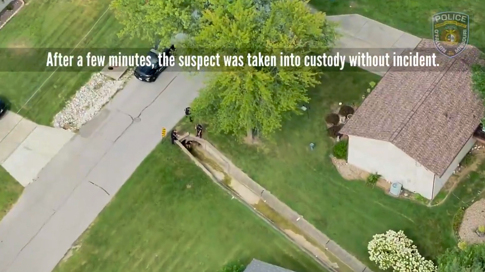 Aerial drone view of officers and vehicles on a suburban street as the suspect is taken into custody, with an on-screen caption from police video.
