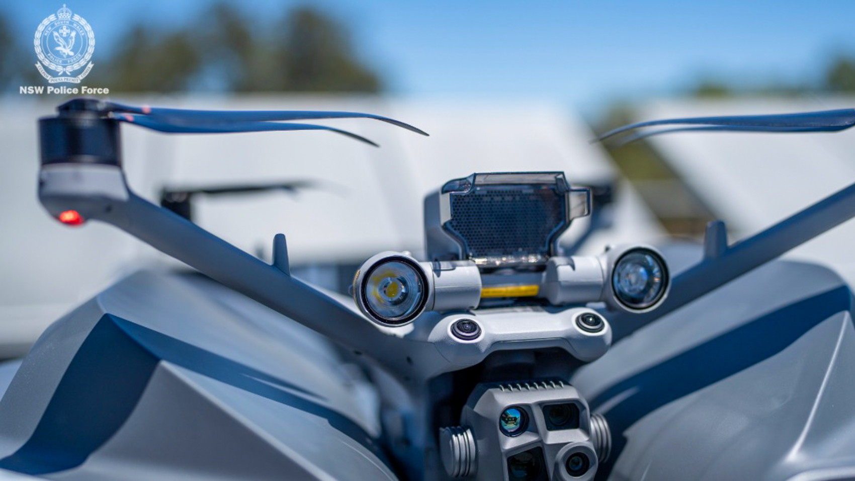 Close-up of the sensor package on a gray police drone, showing a spotlight, cameras, and gimbal optics.