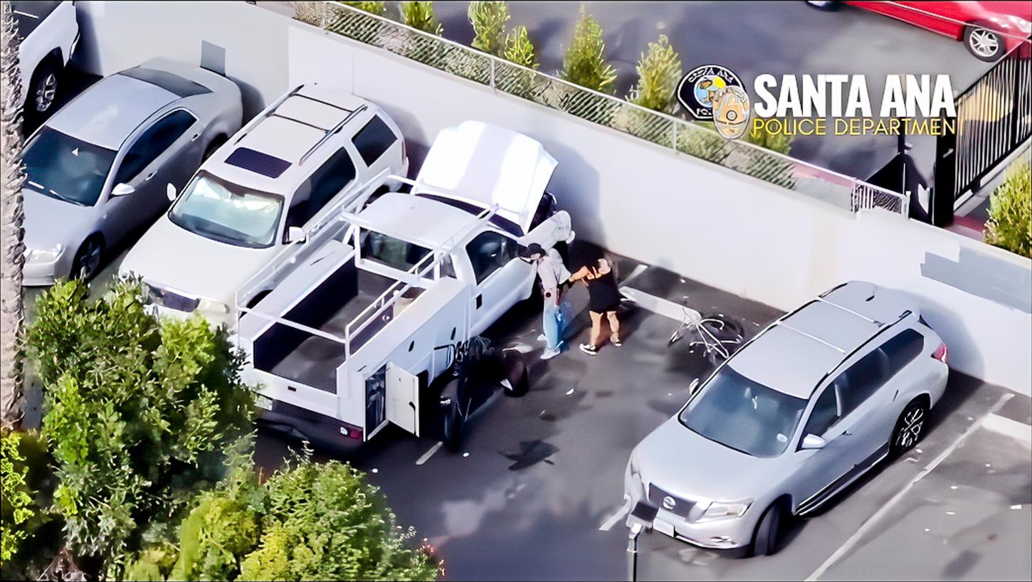 Aerial drone view of two suspects moving property beside a white work truck in a parking lot, with the Santa Ana Police Department watermark.