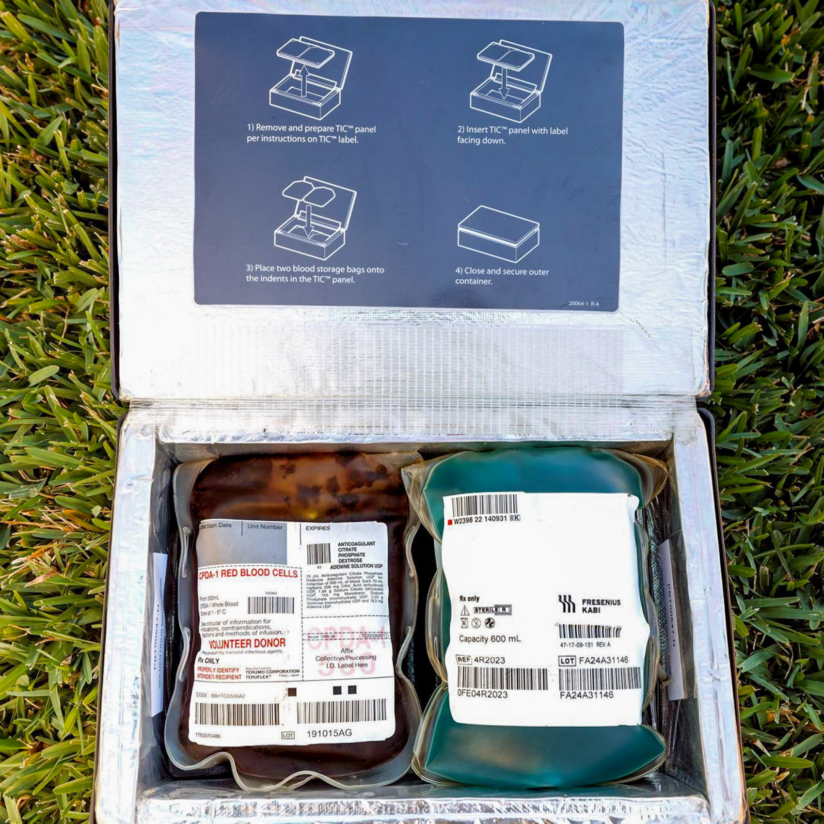 An open insulated transport case on grass holding two blood storage bags next to printed packing instructions